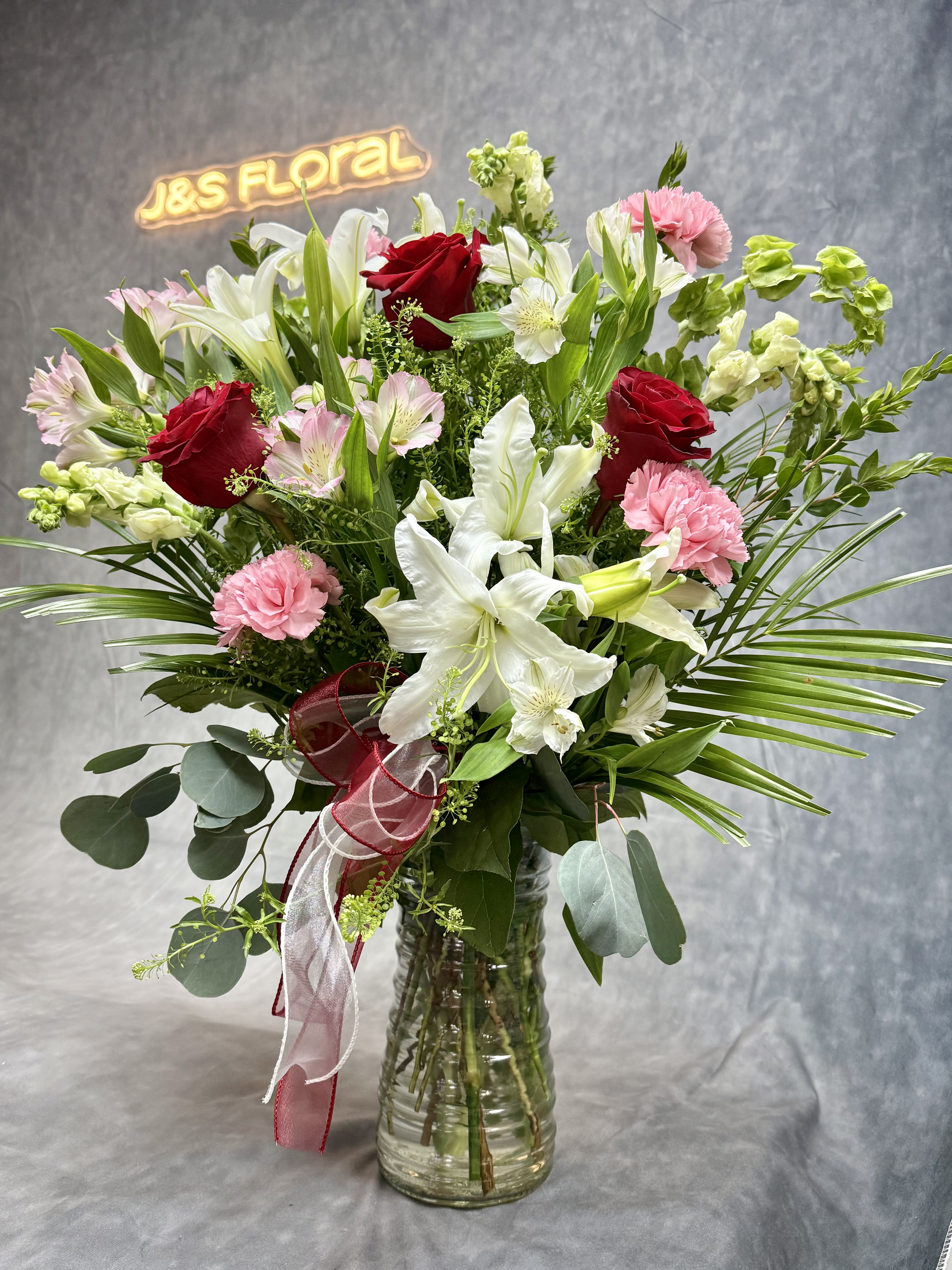 Mixed bouquet of red roses, white lilies, and pink carnations in a glass vase