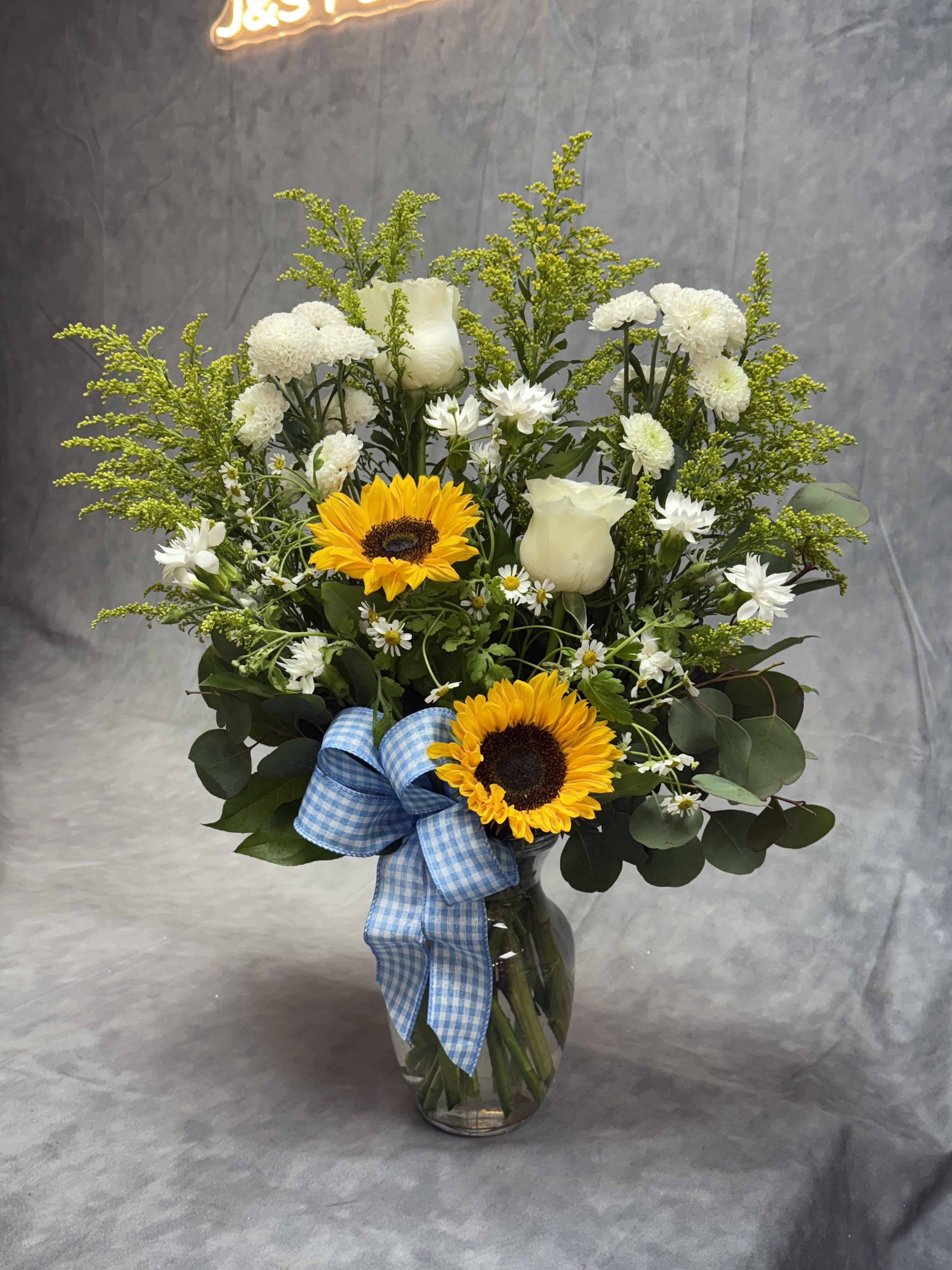 Sunflower and white rose bouquet in a glass vase with a blue ribbon