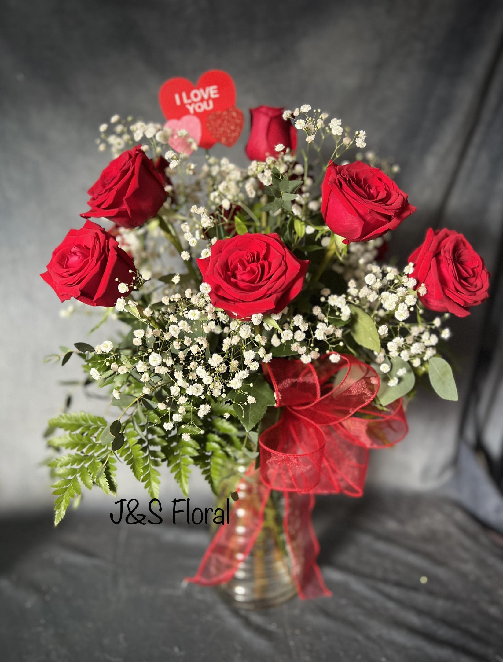 Red roses in a glass vase with baby's breath and a red ribbon