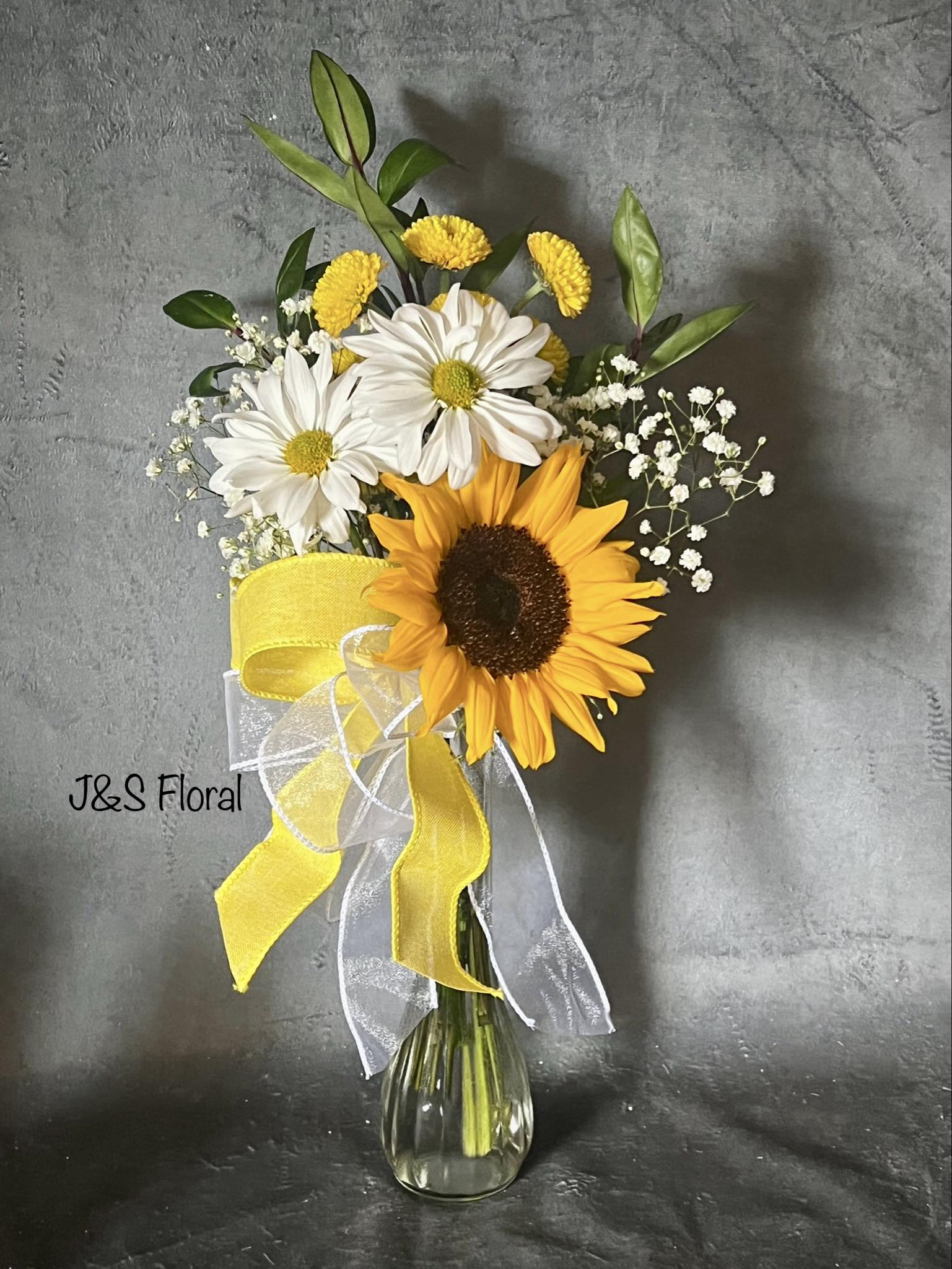 Sunflower and white daisy bouquet in a glass vase with yellow ribbon