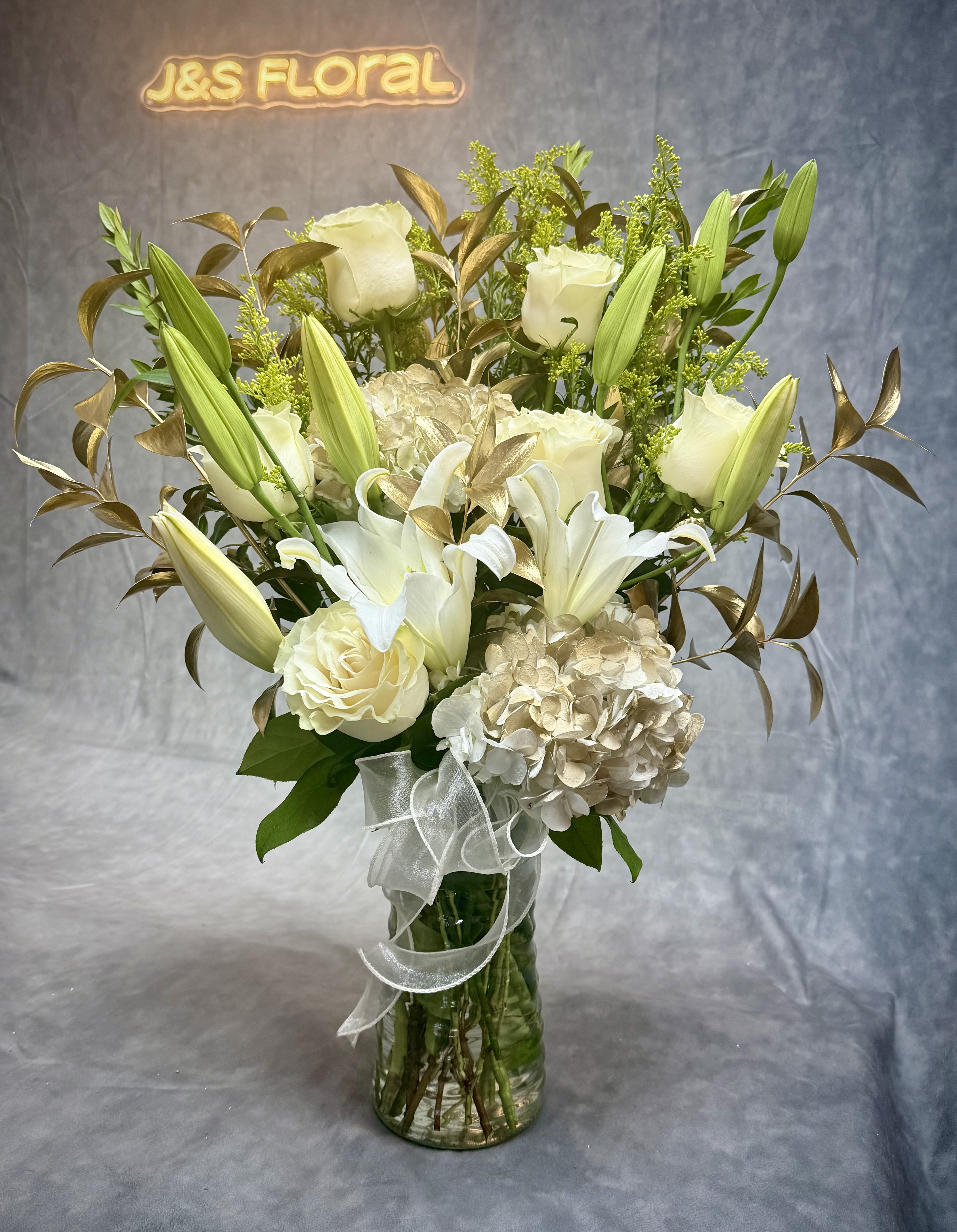 White lilies and roses arranged in a glass vase with a ribbon