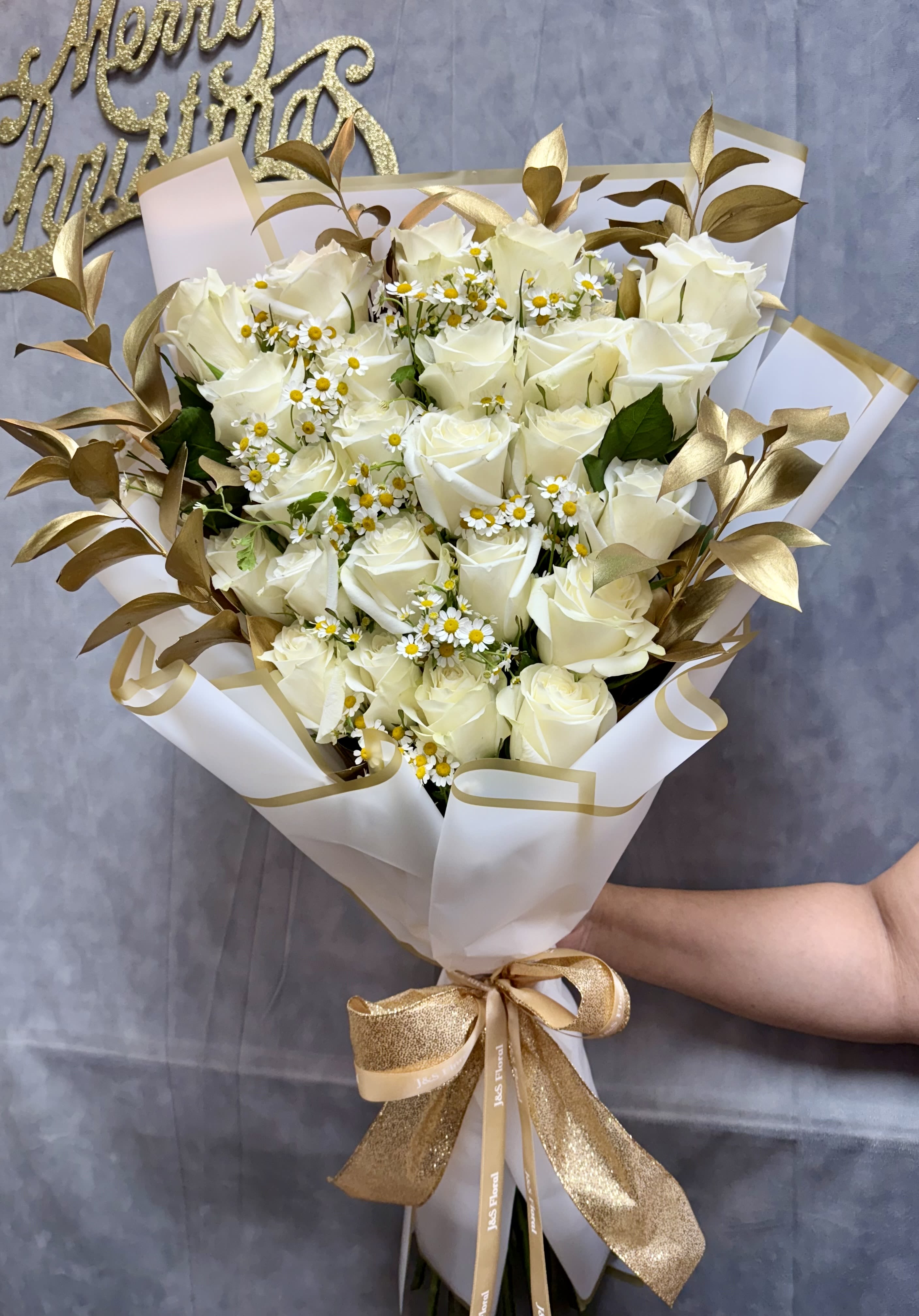 Bouquet of white roses and small daisy-like flowers wrapped in white paper with gold ribbon