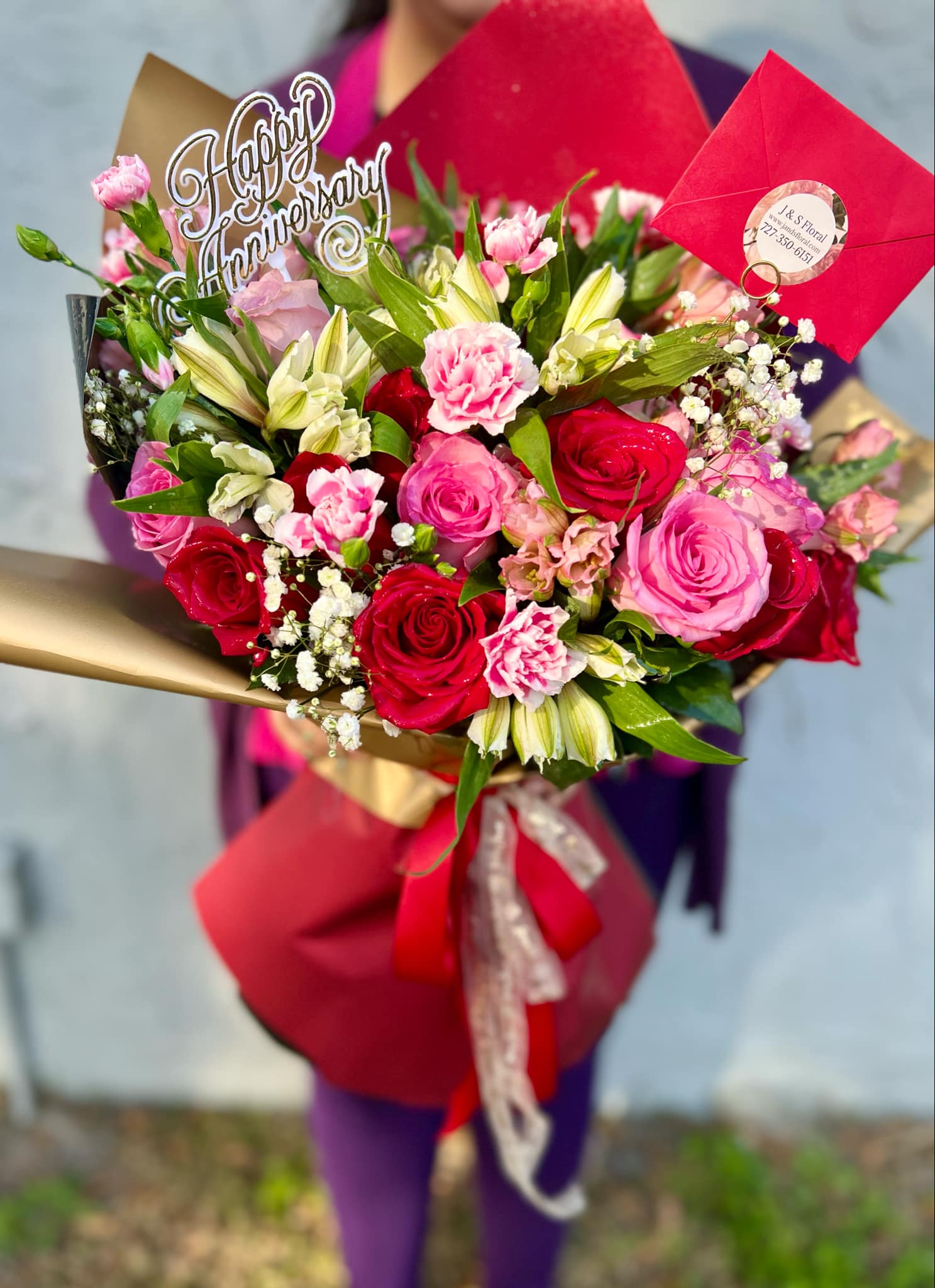 Bouquet of pink and red roses with lilies and carnations, wrapped in red paper