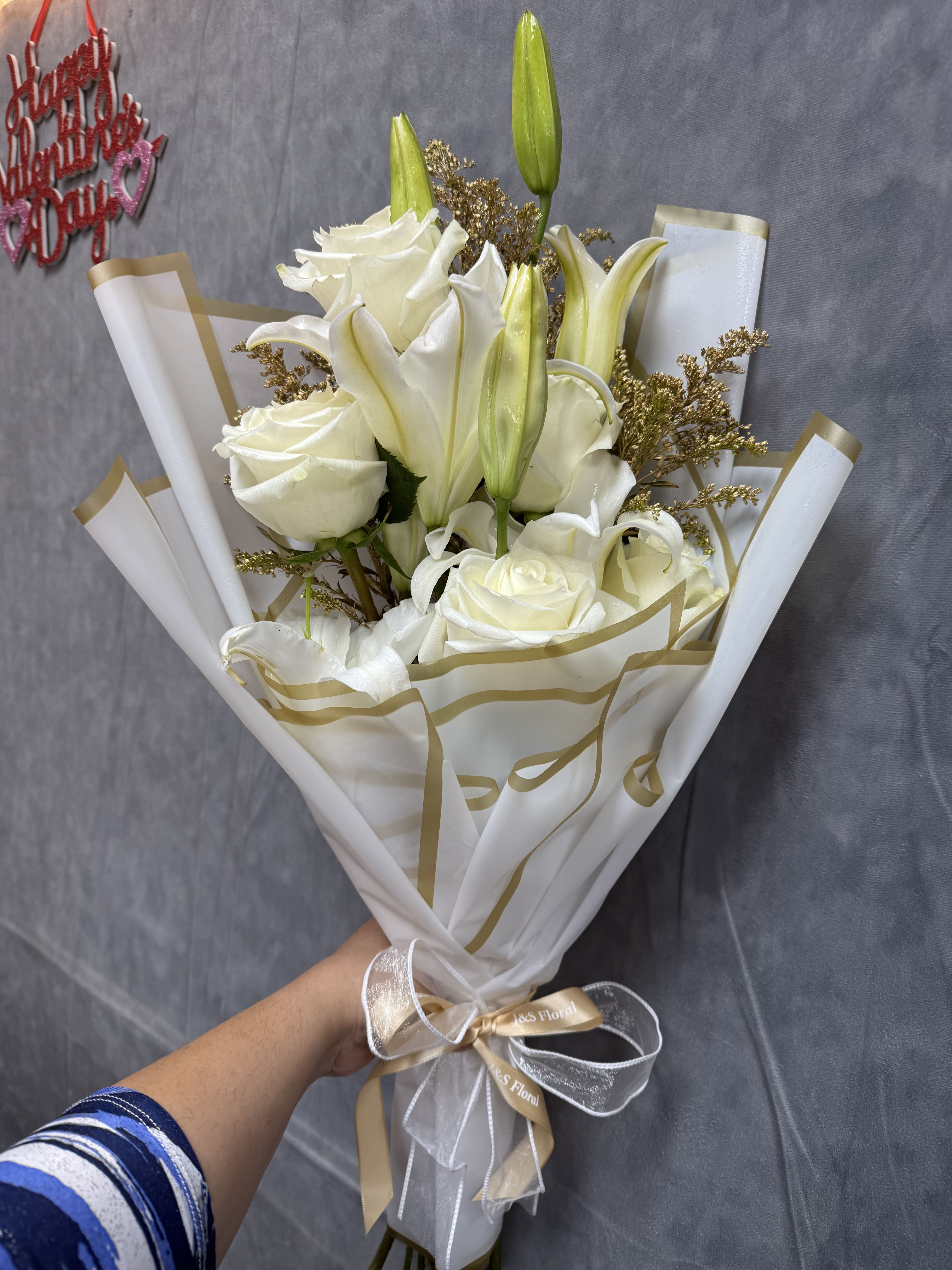 White roses and lilies in wrapped bouquet with gold ribbon