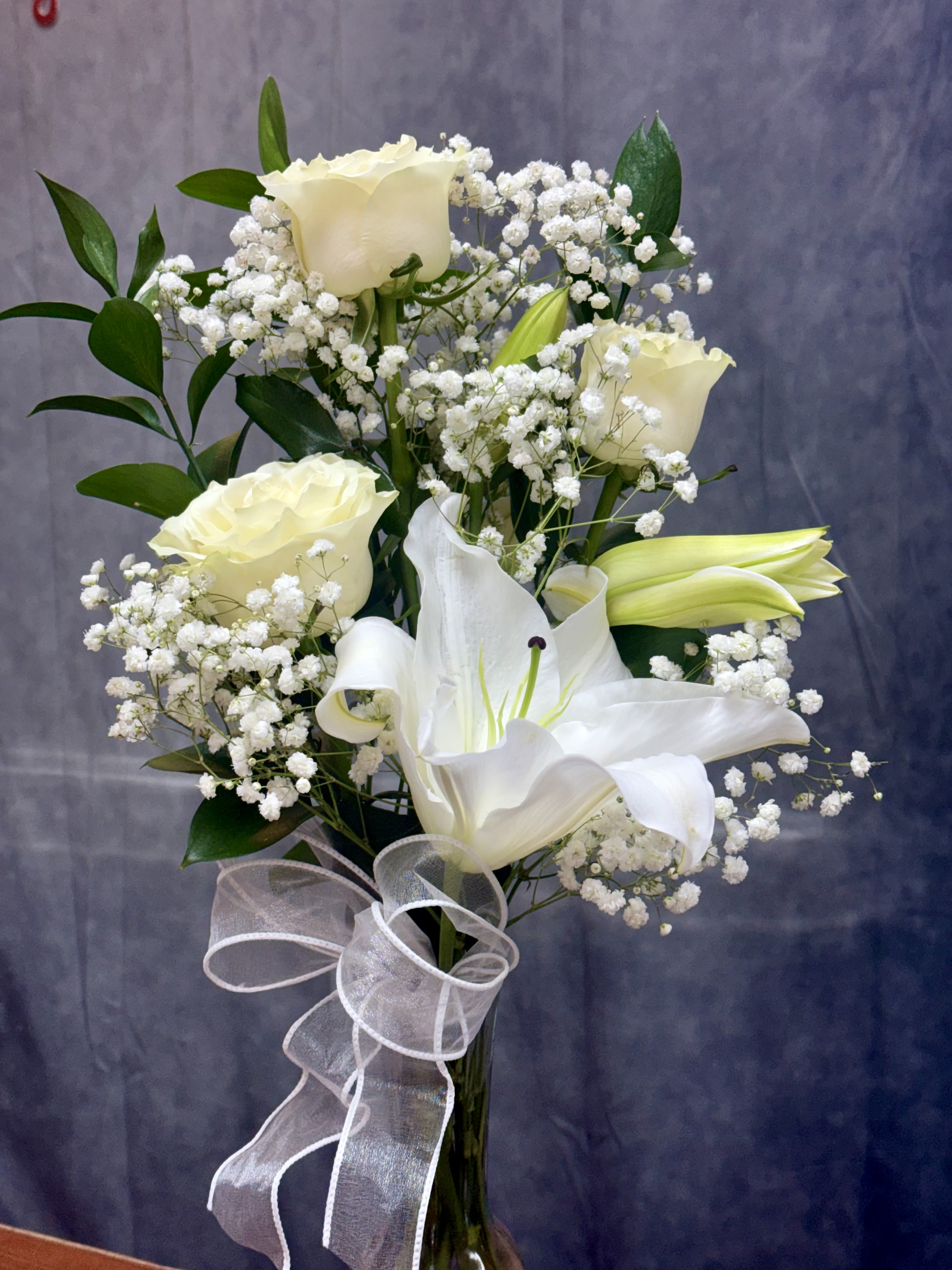 White roses and lilies arranged with baby's breath and a sheer ribbon.