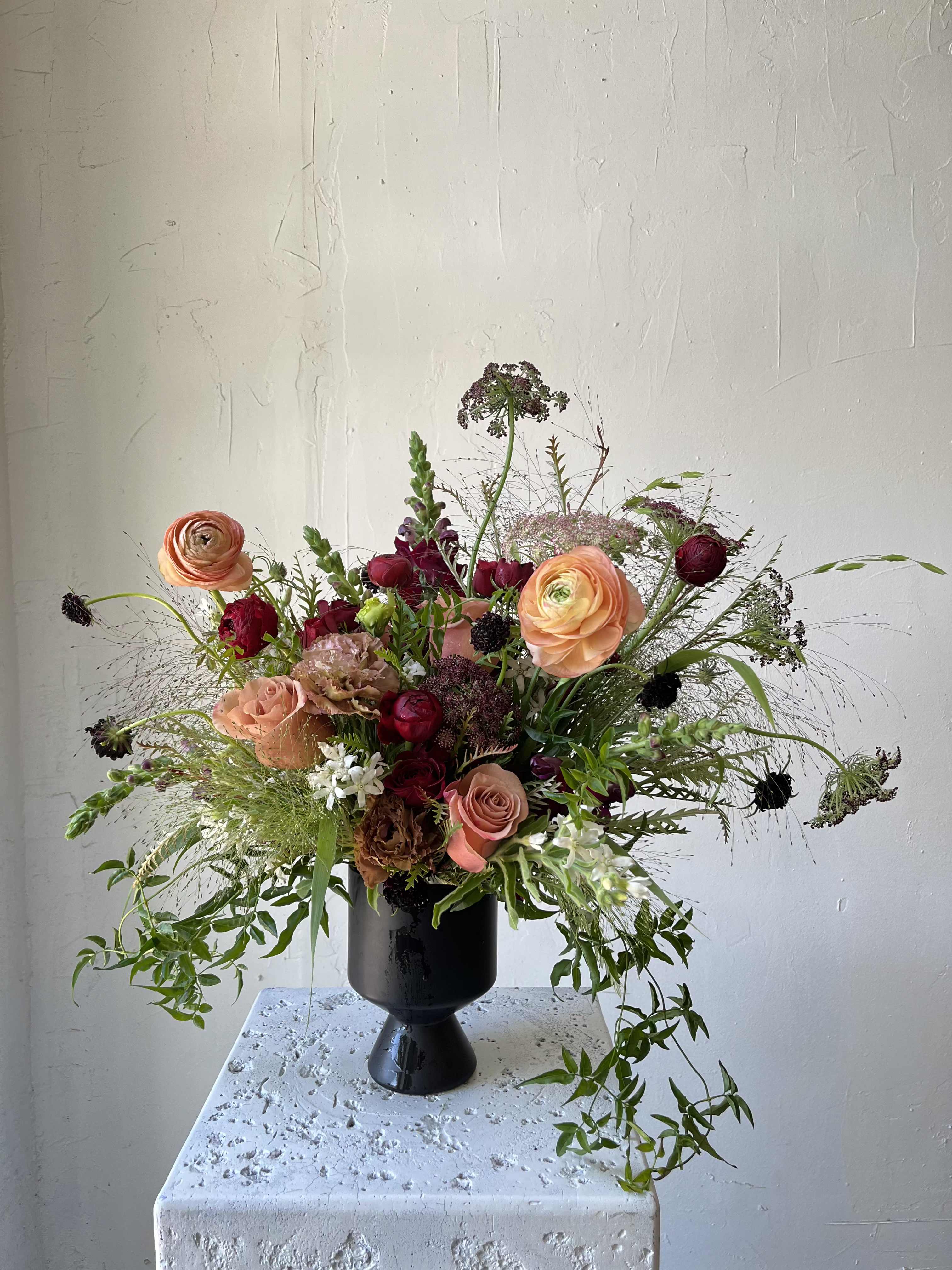 Mixed bouquet of peach and burgundy flowers in a black vase