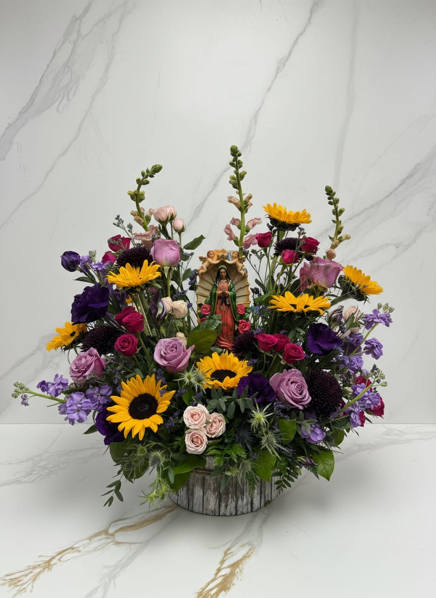 Colorful mixed flower arrangement with a small religious figurine in a rustic container