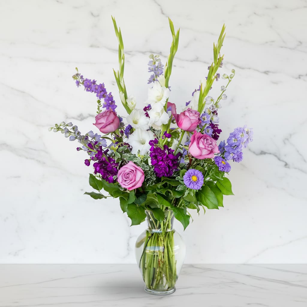 Mixed bouquet of pink roses, white blooms, and purple flowers in a glass vase