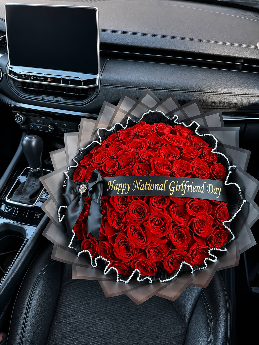 Large bouquet of red roses with a black ribbon and gift banner in a car seat
