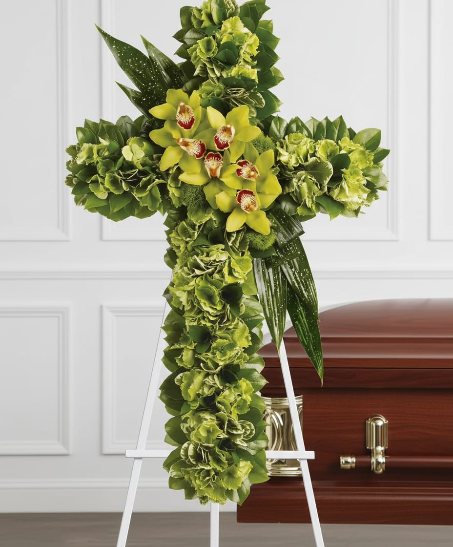 Green floral cross on an easel beside a casket