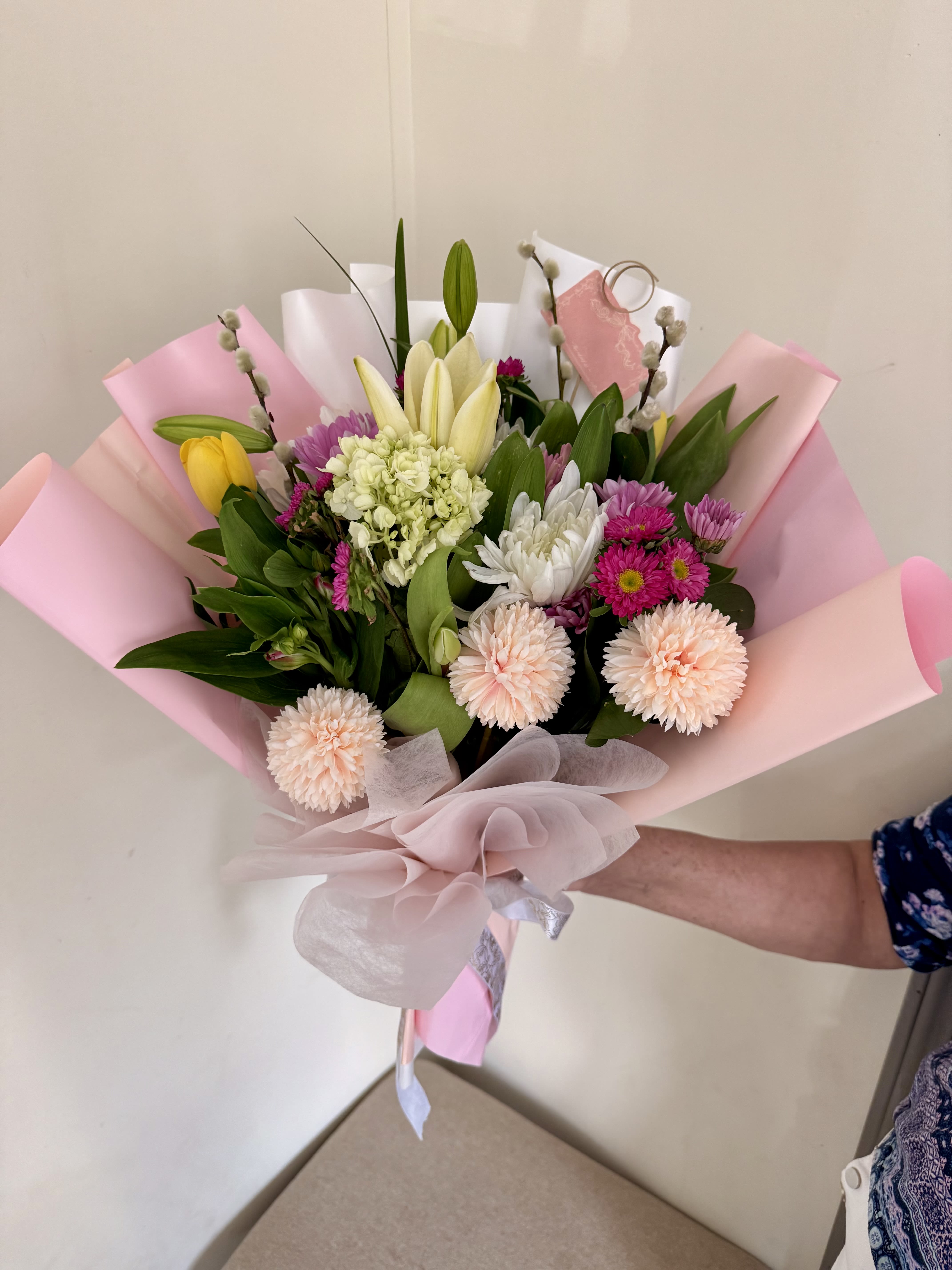 Handheld bouquet of mixed pastel flowers wrapped in pink paper