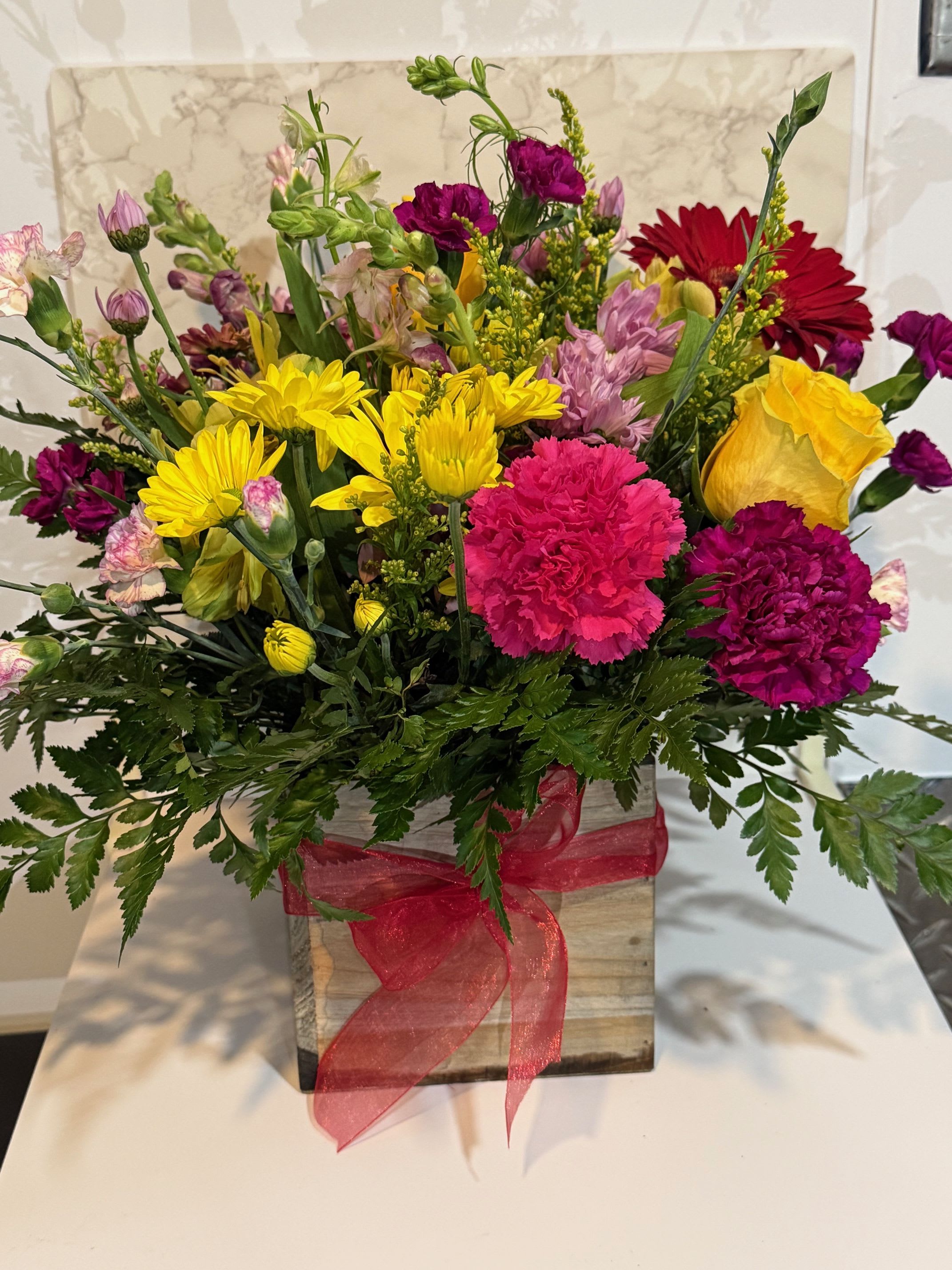 Mixed bouquet in a wooden box with bright yellow, pink, and red flowers