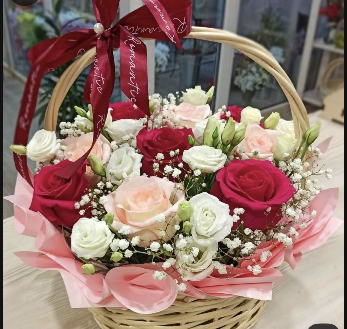Basket of pink, red, and white roses with baby's breath and a red ribbon