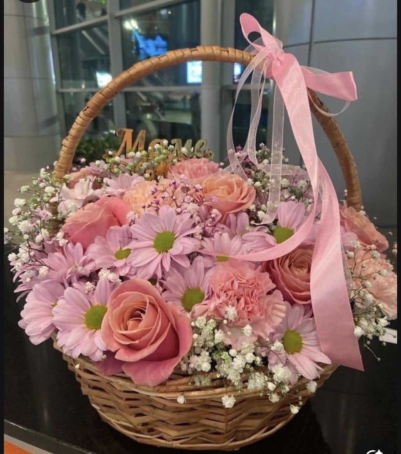 Pink roses and daisies arranged in a wicker basket with a pink ribbon