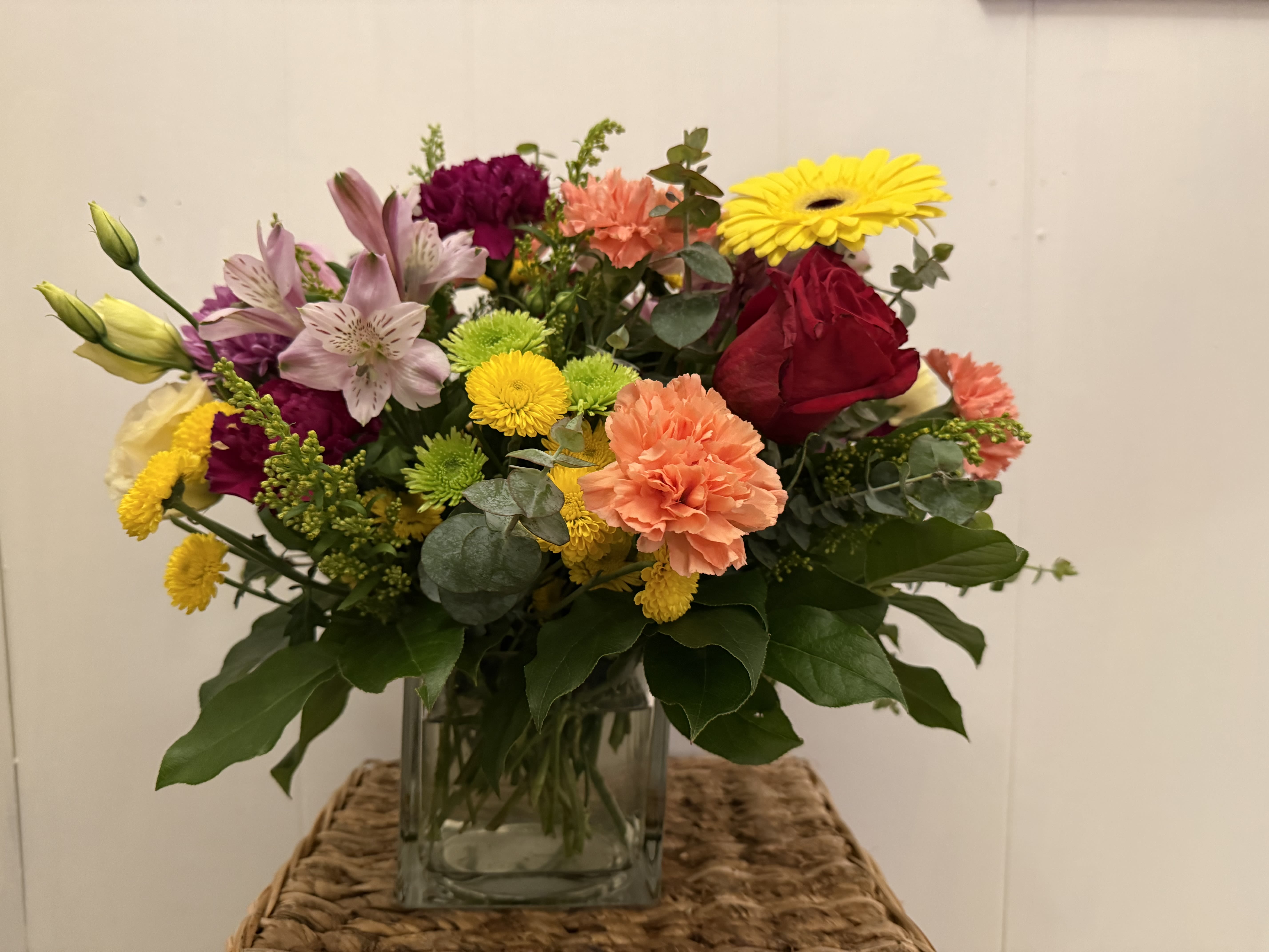 Mixed bouquet in a clear glass vase with roses, lilies, carnations, and daisies