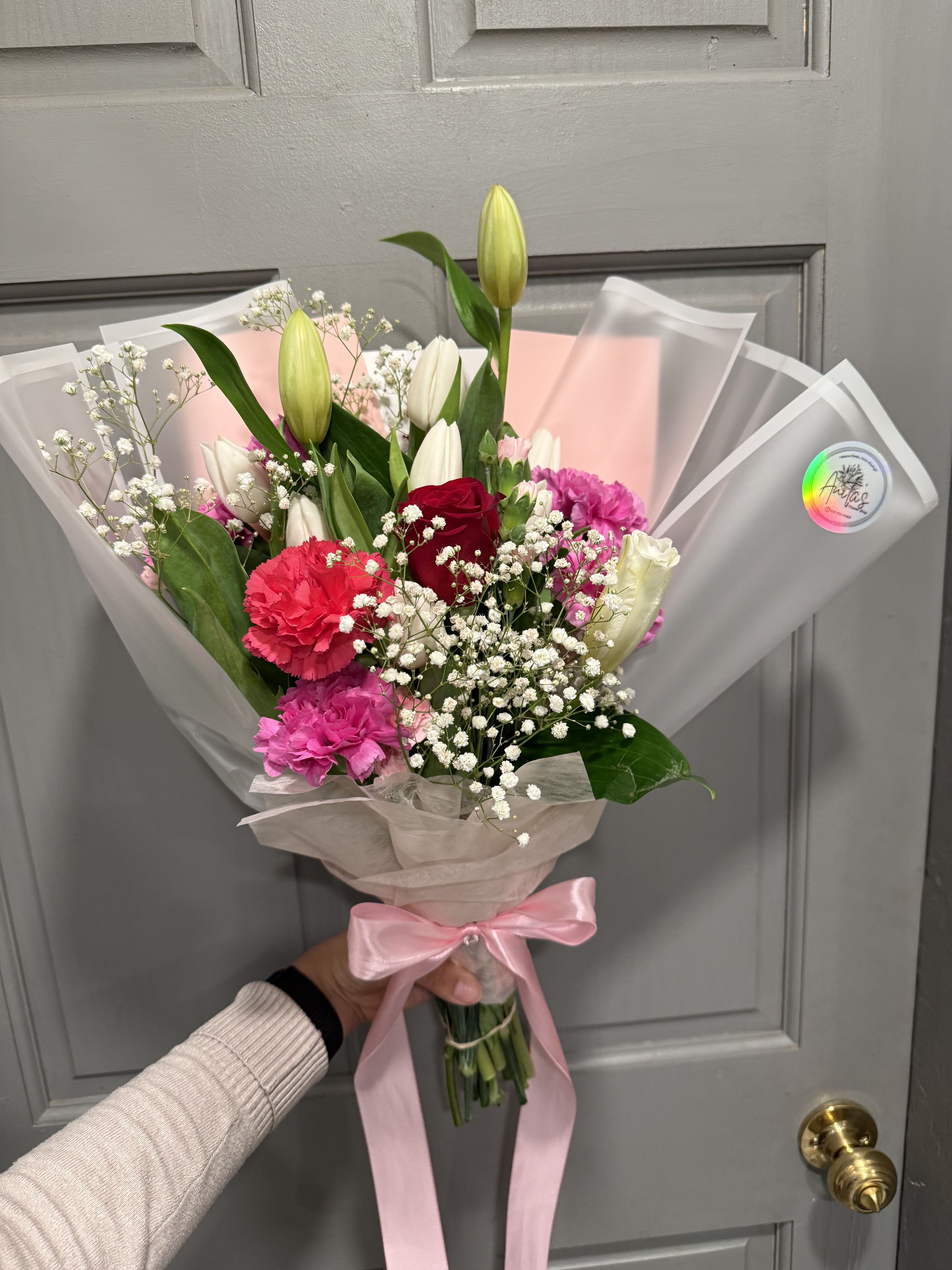 Handheld bouquet of lilies, roses, carnations, and baby's breath wrapped in pink paper