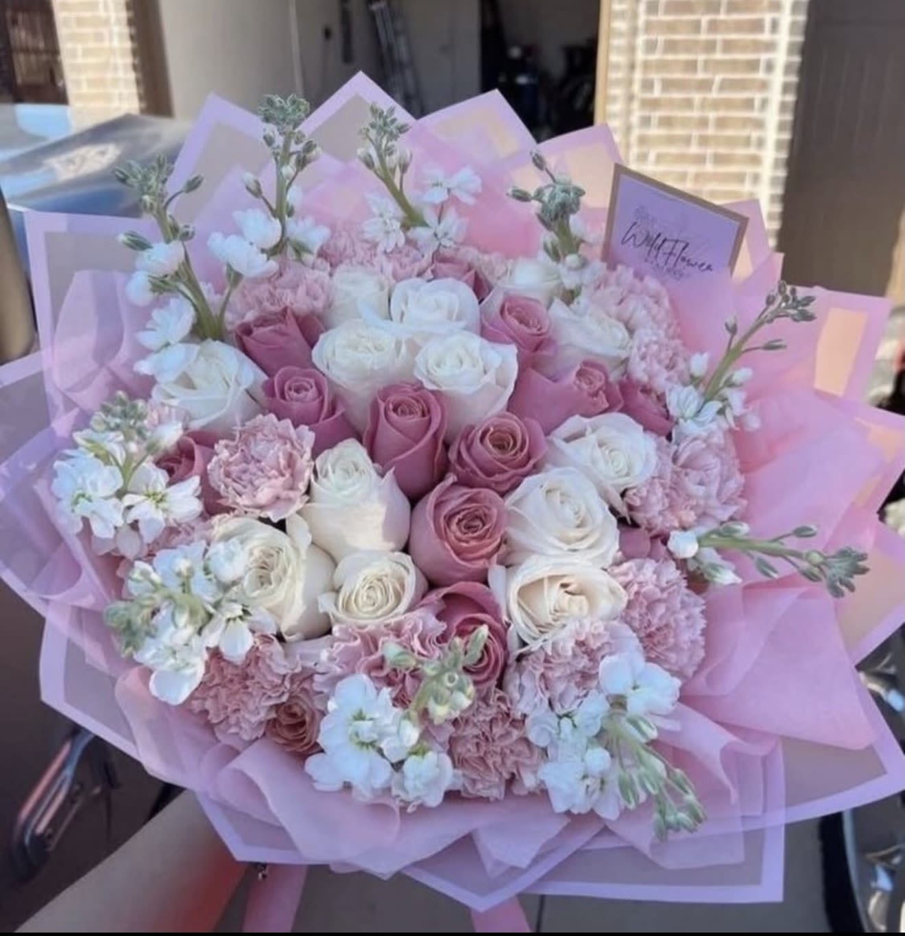 Pink and white rose bouquet with small white blossoms wrapped in pink paper