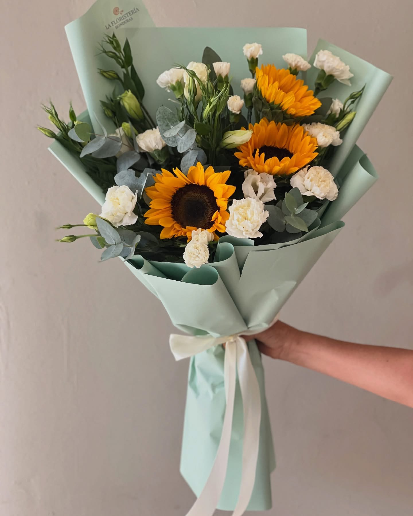 Bouquet of sunflowers and white carnations wrapped in pale mint paper