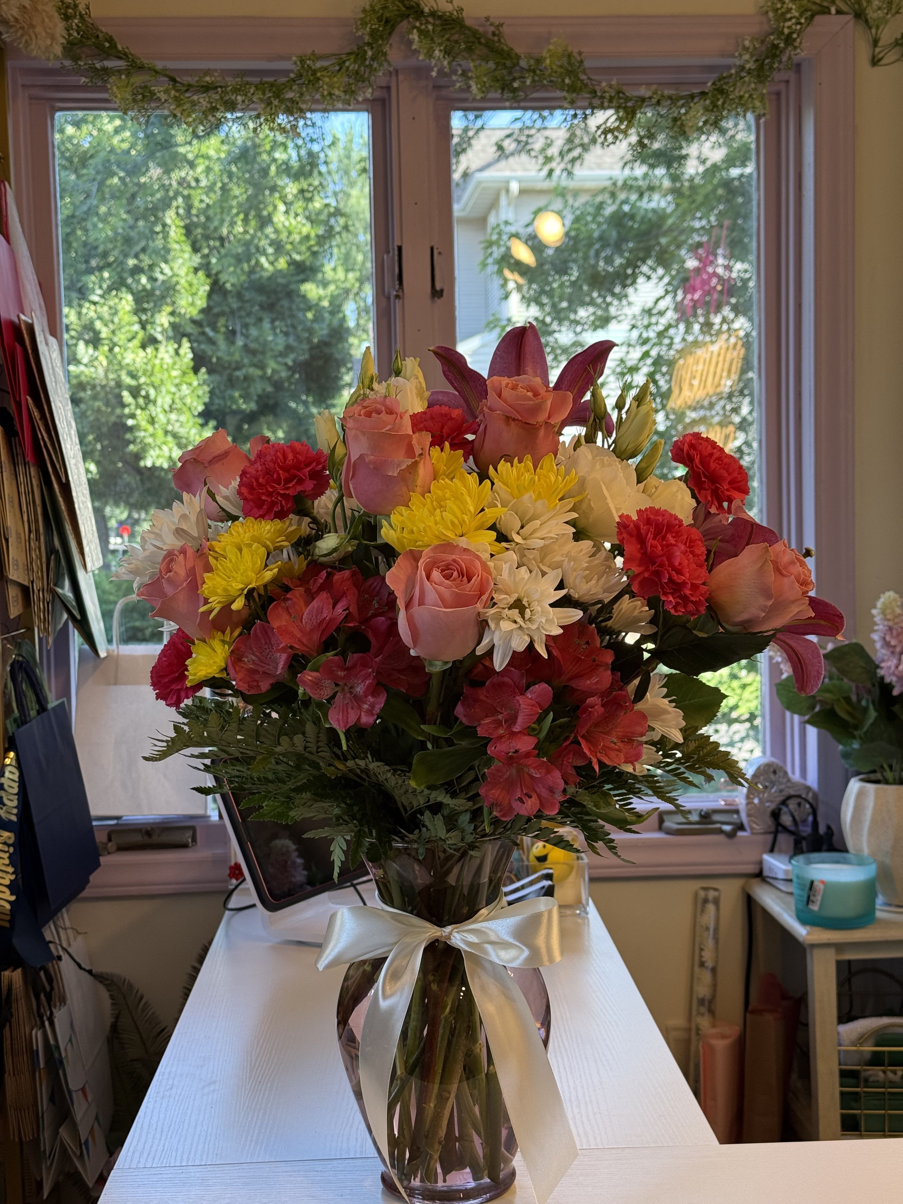 Mixed bouquet of pink roses, yellow and white daisies, and red carnations in a glass vase