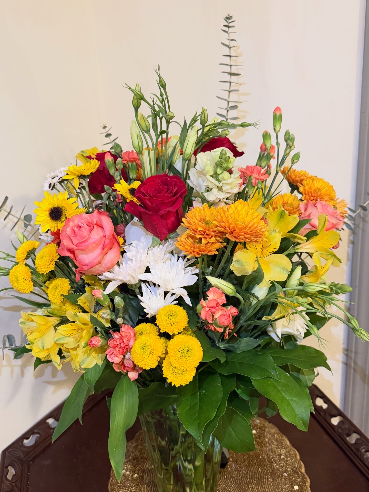 Mixed bouquet of roses, daisies, and yellow blooms in a glass vase