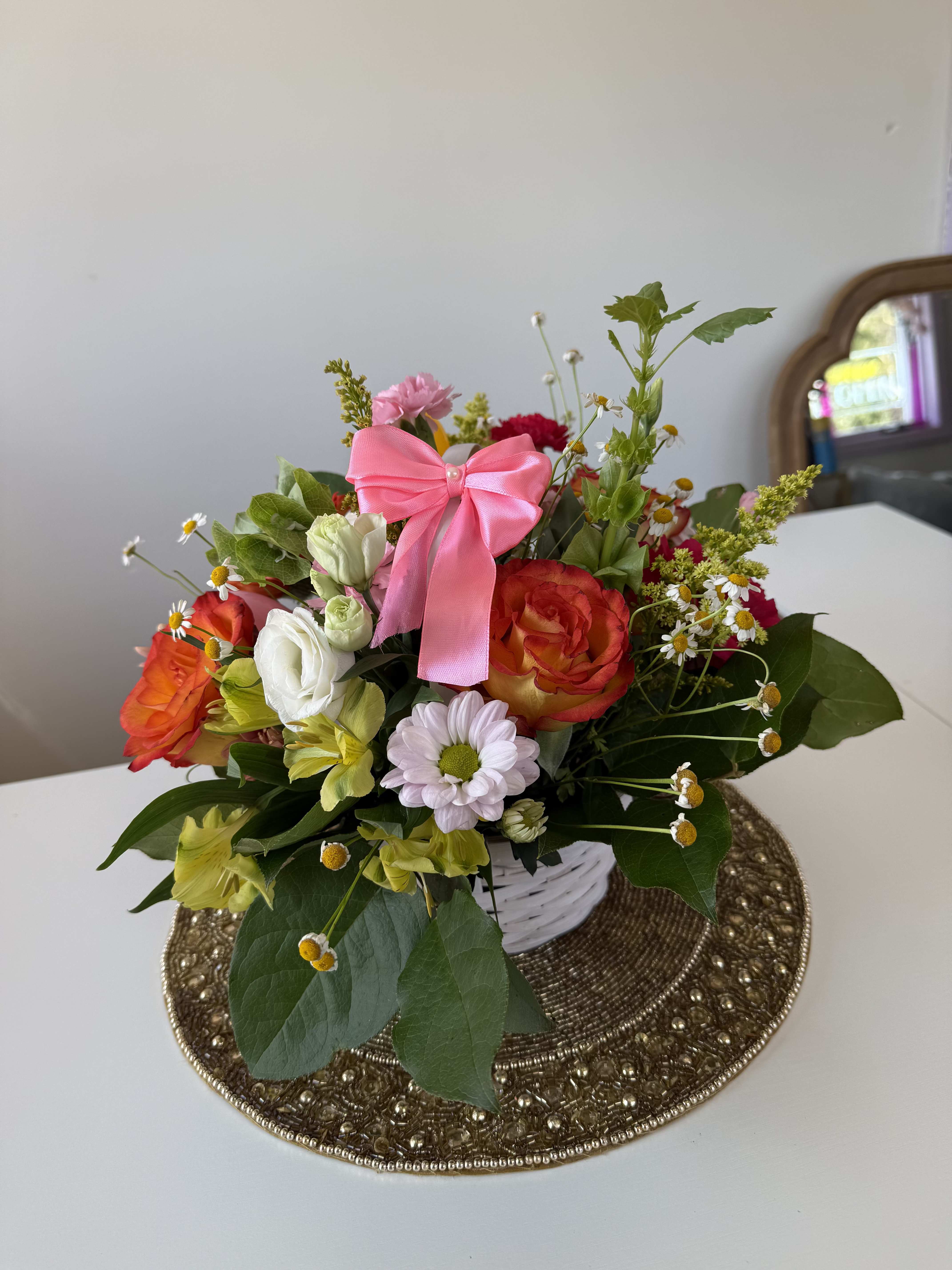 Mixed bouquet of roses, daisies, and alstroemeria in a white basket with a pink bow