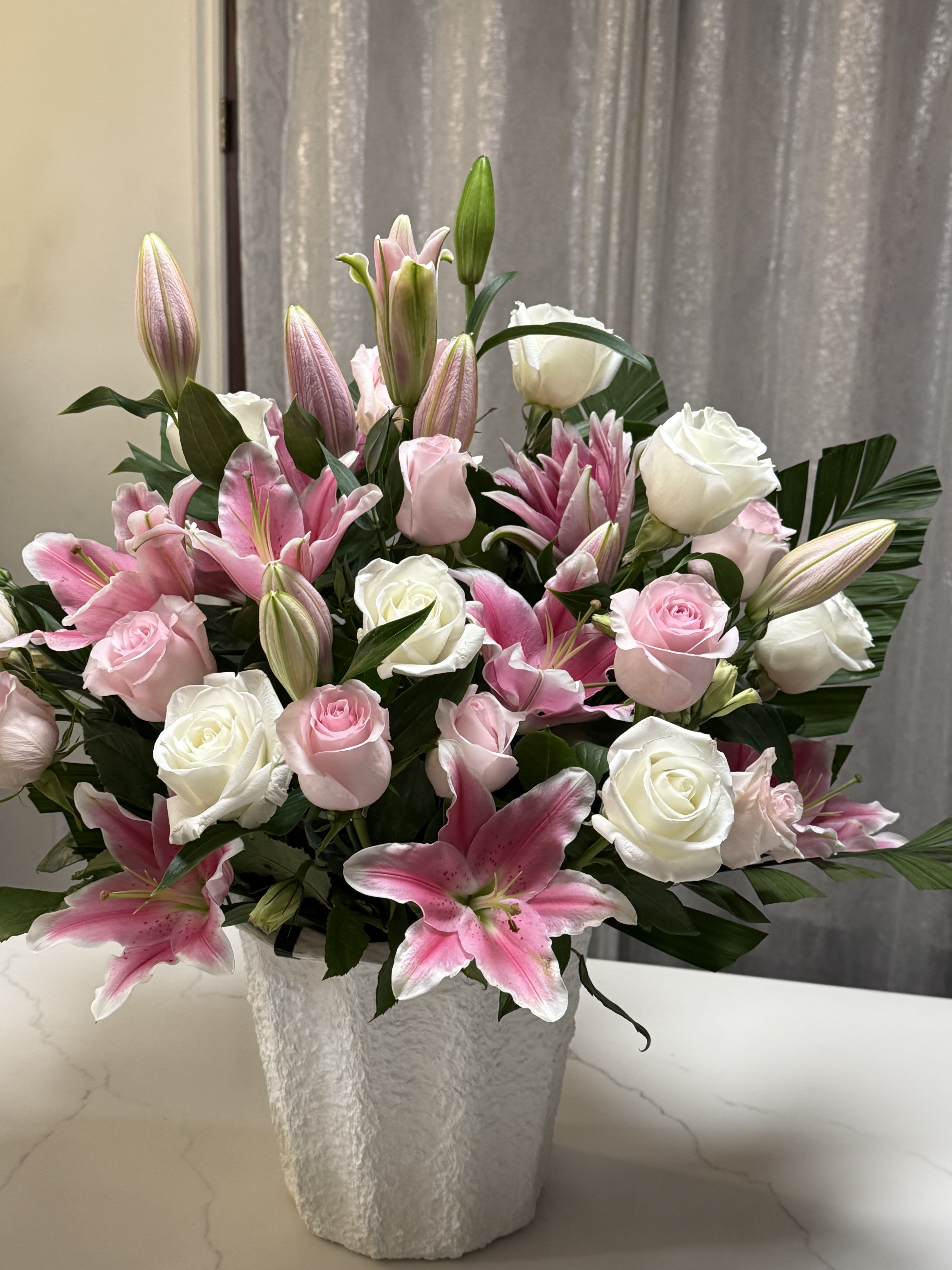 Pink lilies and white roses arranged in a textured white vase