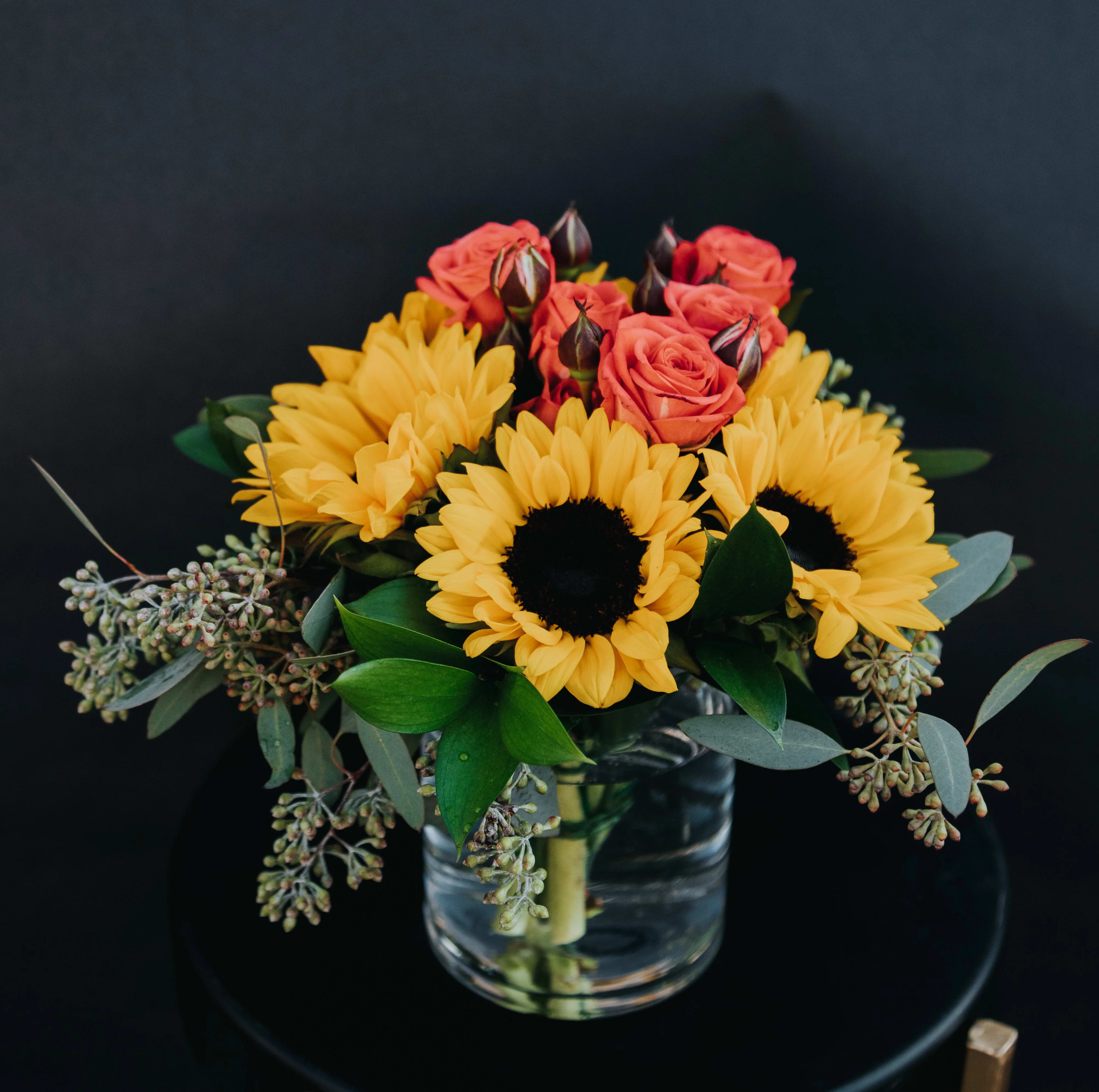 Sunflowers and coral roses arranged in a clear glass vase