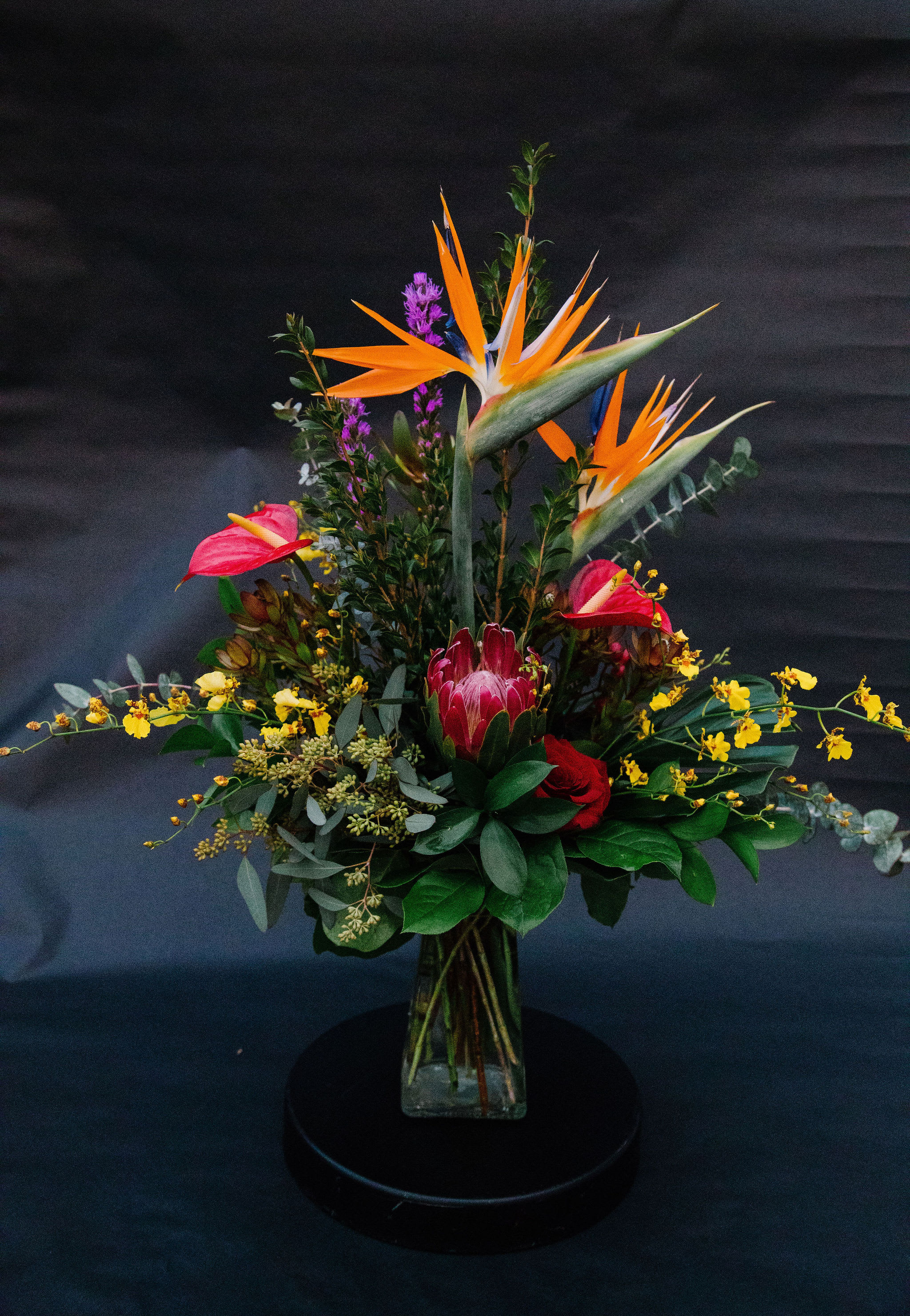 Tropical bouquet with orange bird-of-paradise and pink anthuriums in a glass vase