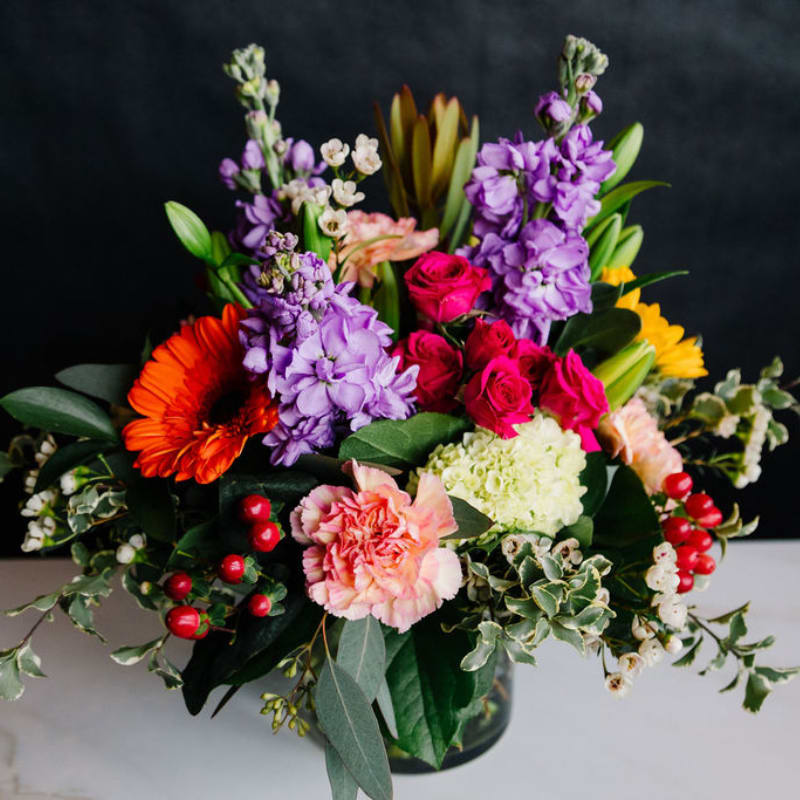 Colorful mixed bouquet in a glass vase with roses, lilies, and gerbera daisies