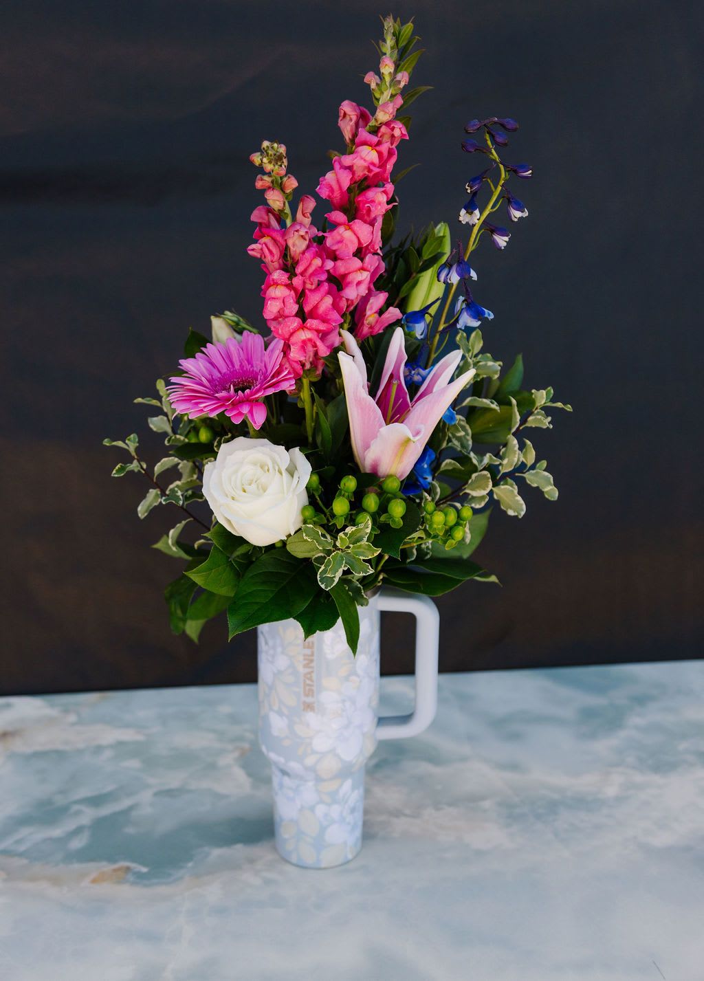 Mom's Garden Tumber - A vibrant, garden-inspired arrangement featuring bold seasonal blooms, layered textures, and lush greenery. Designed with height and movement, this piece brings a fresh, artful energy—perfect for celebrating life’s brightest moments.  Order Now! Each tumbler is a one-of-a-kind, hand-painted piece sealed with a clear gloss powder coat—dishwasher safe, chip-resistant, and made to last; by artist Melanie Haggard @meligrafi. Want the tumbler without flowers? Just click the “Gift” tab at the top of the page.