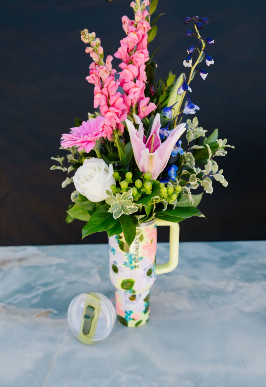 Garden Glow - A fresh, garden-inspired mix of seasonal blooms in soft pinks, whites, and vibrant accents, thoughtfully arranged in a hand-painted Stanley tumbler. Designed to delight now and carry her through every day after, this piece blends beautiful florals with a keepsake she’ll reach for again and again.  Order Now! Each tumbler is a one-of-a-kind, hand-painted piece sealed with a clear gloss powder coat—dishwasher safe, chip-resistant, and made to last; by artist Melanie Haggard @meligrafi. Want the tumbler without flowers? Just click the “Gift” tab at the top of the page.