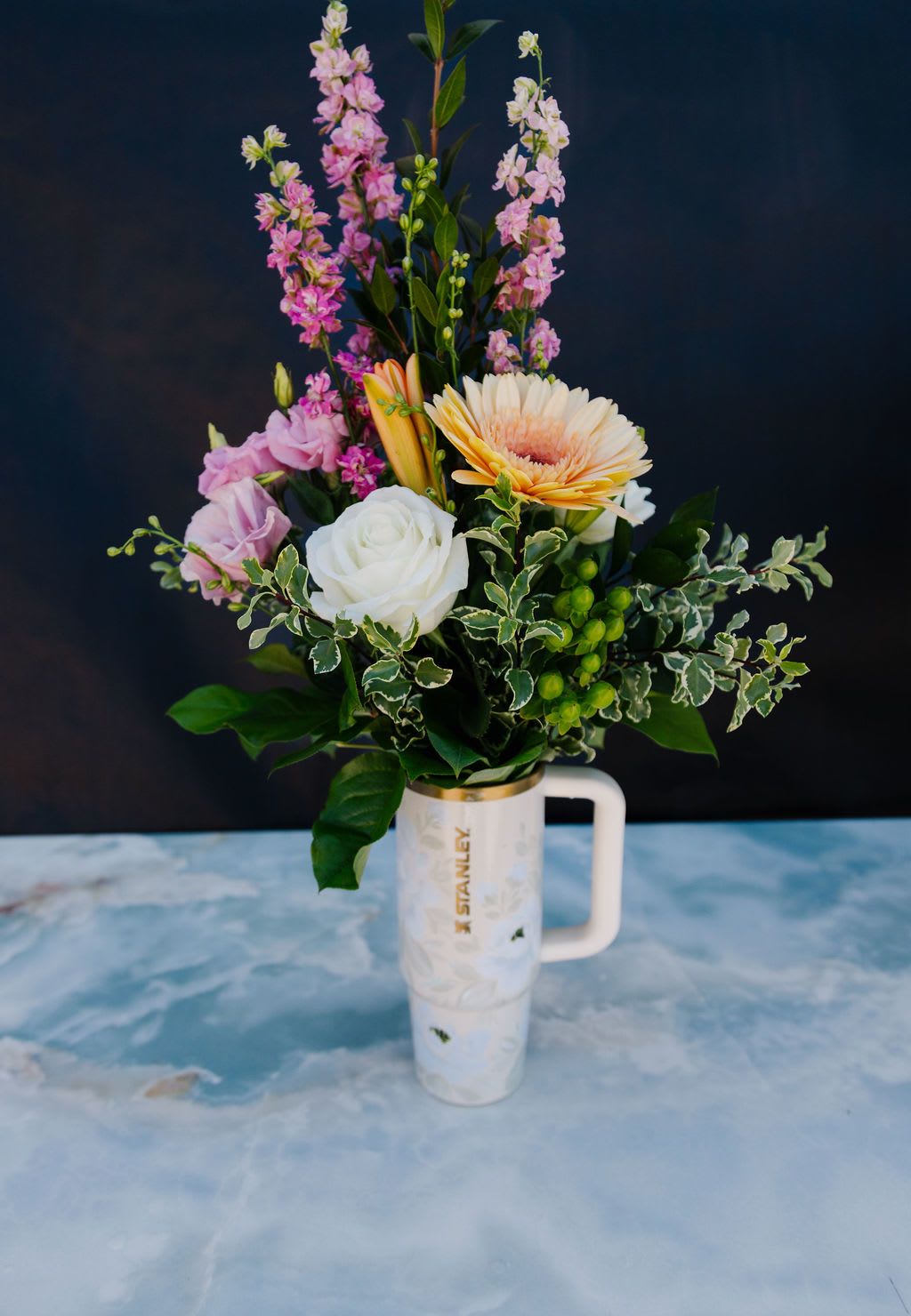 Morning Blooms - A soft, garden-inspired mix of seasonal blooms in blush, ivory, and gentle pastel tones, thoughtfully arranged in a hand-painted Mother’s Day tumbler. Designed to feel fresh and refined, this piece pairs beautiful florals with a keepsake she’ll enjoy long after the blooms have faded.  Order Now! Each tumbler is a one-of-a-kind, hand-painted piece sealed with a clear gloss powder coat—dishwasher safe, chip-resistant, and made to last; by artist Melanie Haggard @meligrafi. Want the tumbler without flowers? Just click the “Gift” tab at the top of the page.