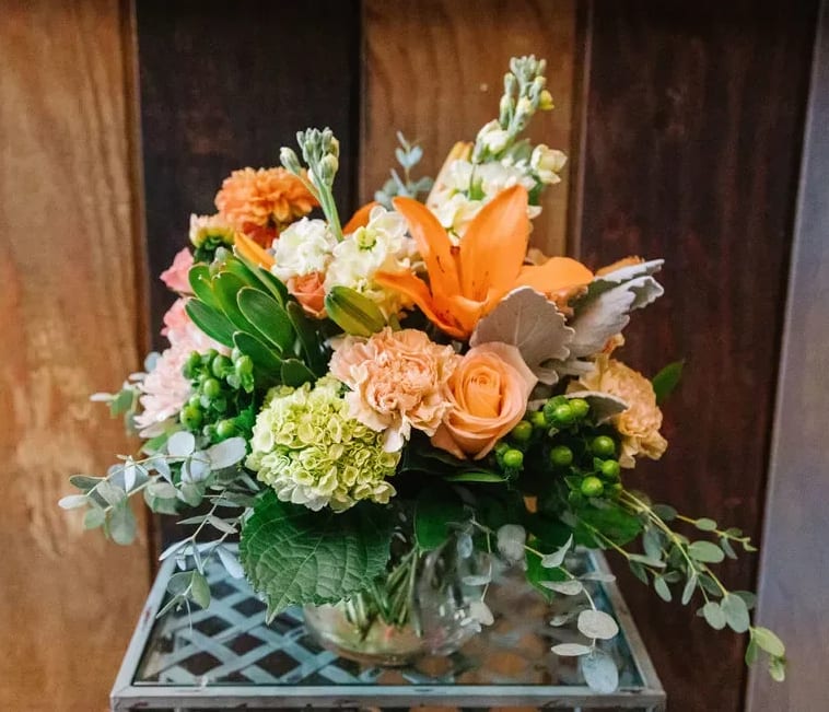 Mixed bouquet with orange lilies, peach roses, and green hydrangeas in a glass vase