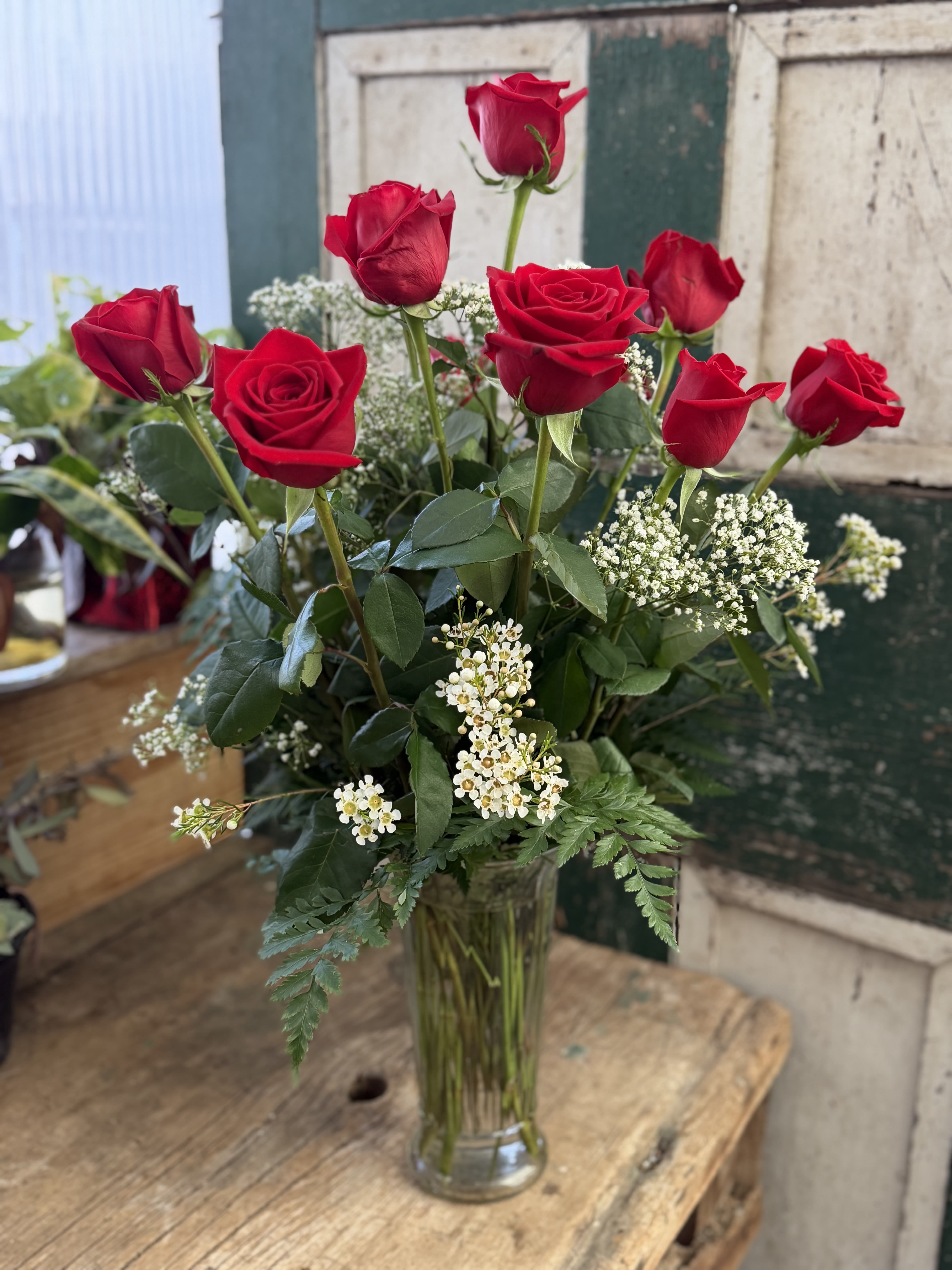 A Dozen Deluxe Roses - Velvety long-stemmed red roses rise in a clean clear glass vase, the classic anniversary bouquet that says love and romance without saying a word. The tall, vertical profile and rich red petals are softened by clusters of delicate white filler blooms and fresh green foliage, creating a timeless arrangement perfect for anniversaries, Valentine's Day, or a meaningful "I'm sorry."  This dozen-rose arrangement combines evenly spaced stems for a balanced, elegant silhouette with small white accents that add texture and light. Presented in a simple clear glass vase, it suits birthdays, Mother's Day, winter celebrations, or just-because surprises-any moment when you want the recipient to feel truly seen and cherished.  Choose this arrangement when you want to celebrate love, repair a relationship, or mark a special birthday with something that feels both classic and thoughtfully composed. The long-stemmed design creates a striking centerpiece and arrives ready to display; include a short, heartfelt note to make the sentiment unforgettable.