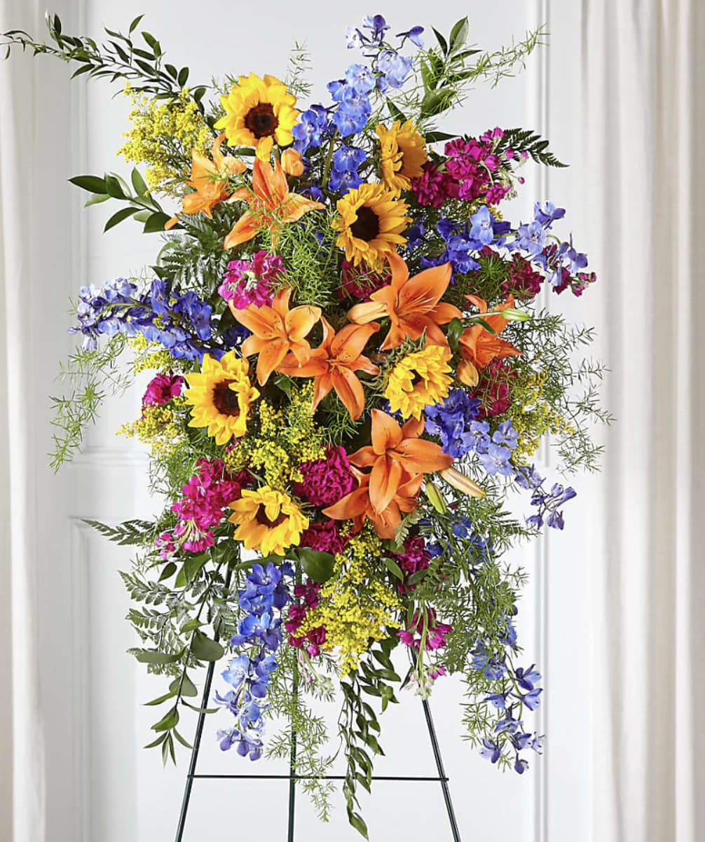 Tall standing arrangement with sunflowers, lilies, and blue flowers