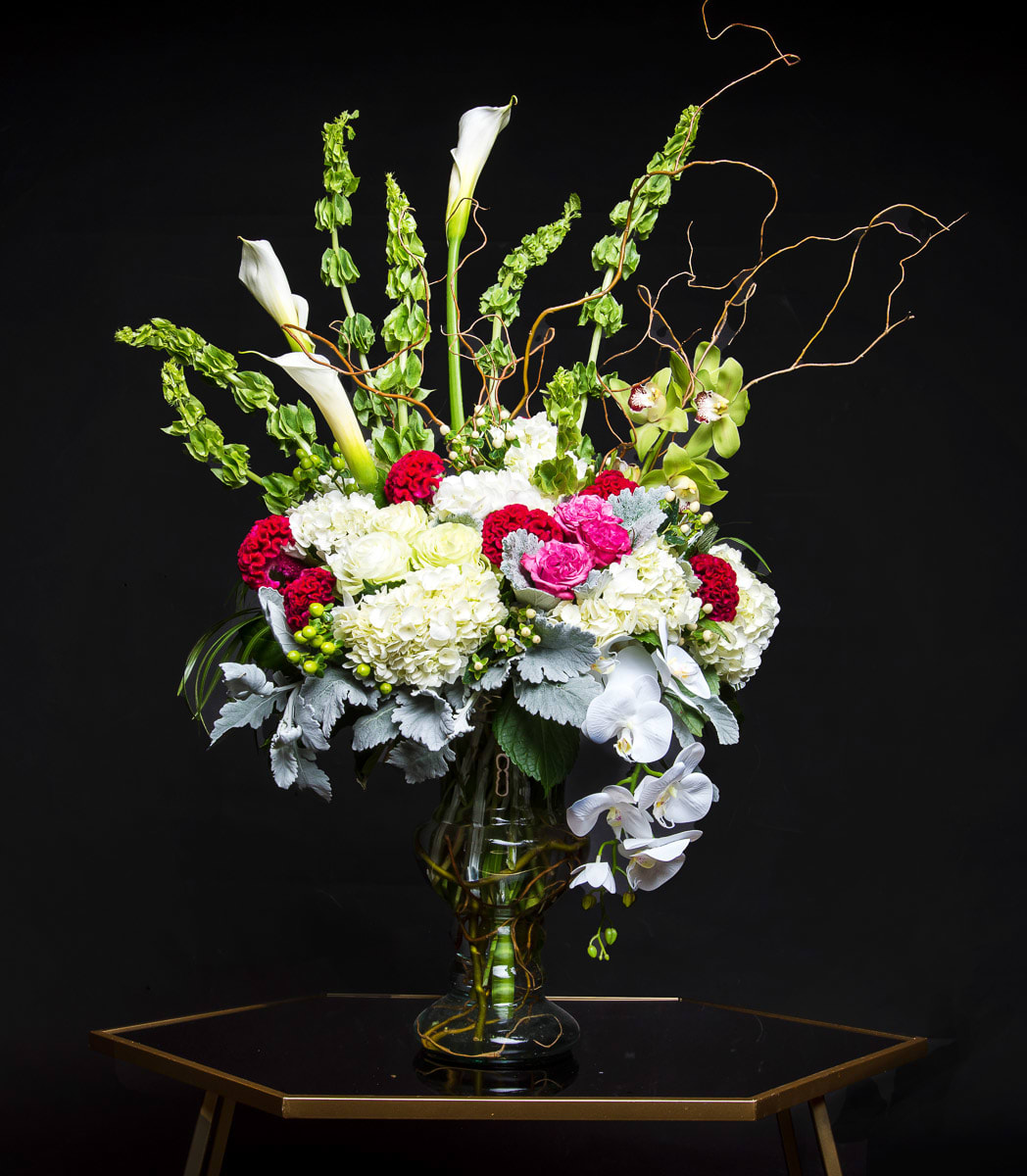 Tall floral arrangement in a glass vase with white calla lilies and orchids