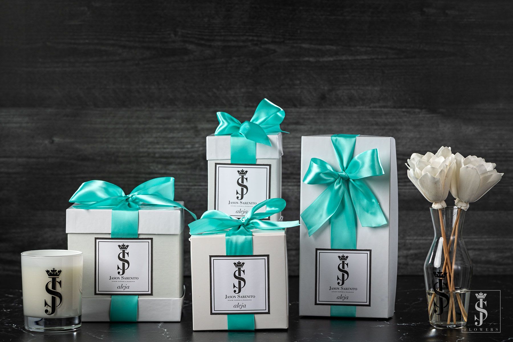 Gift boxes with teal ribbons beside a candle and a small vase of white flowers