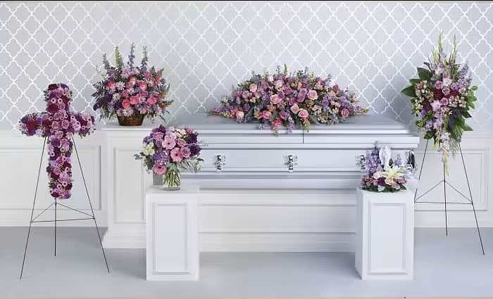 Purple and pink floral funeral casket spray with matching standing arrangements