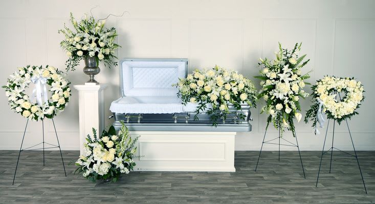White floral funeral casket spray with matching wreaths and standing sprays