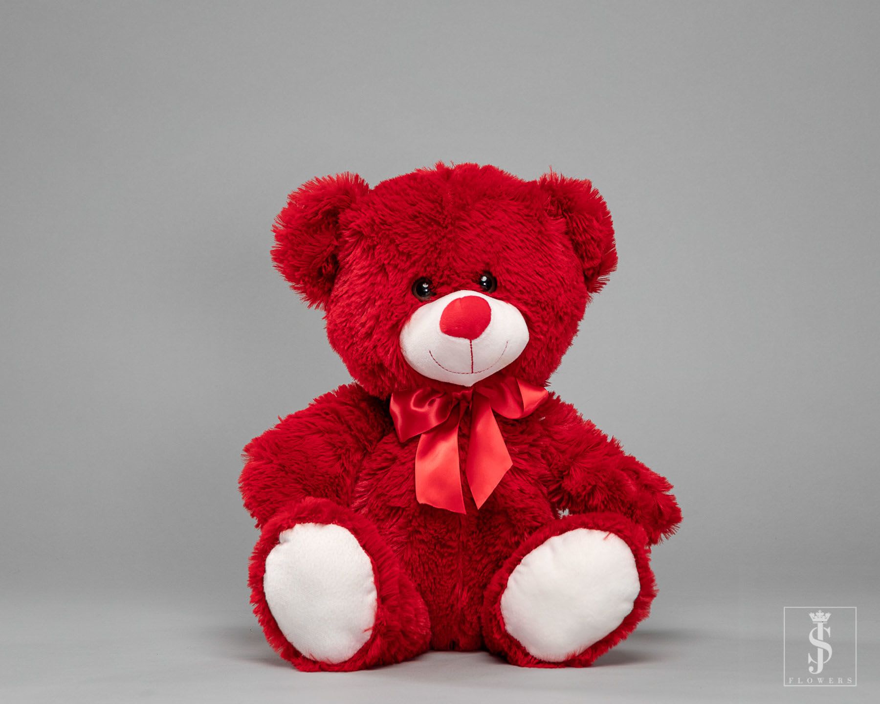 Red teddy bear with a satin bow on a gray background