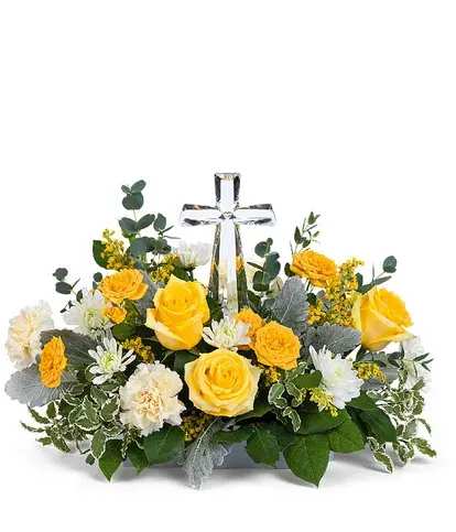 Yellow roses and white flowers arranged around a clear glass cross