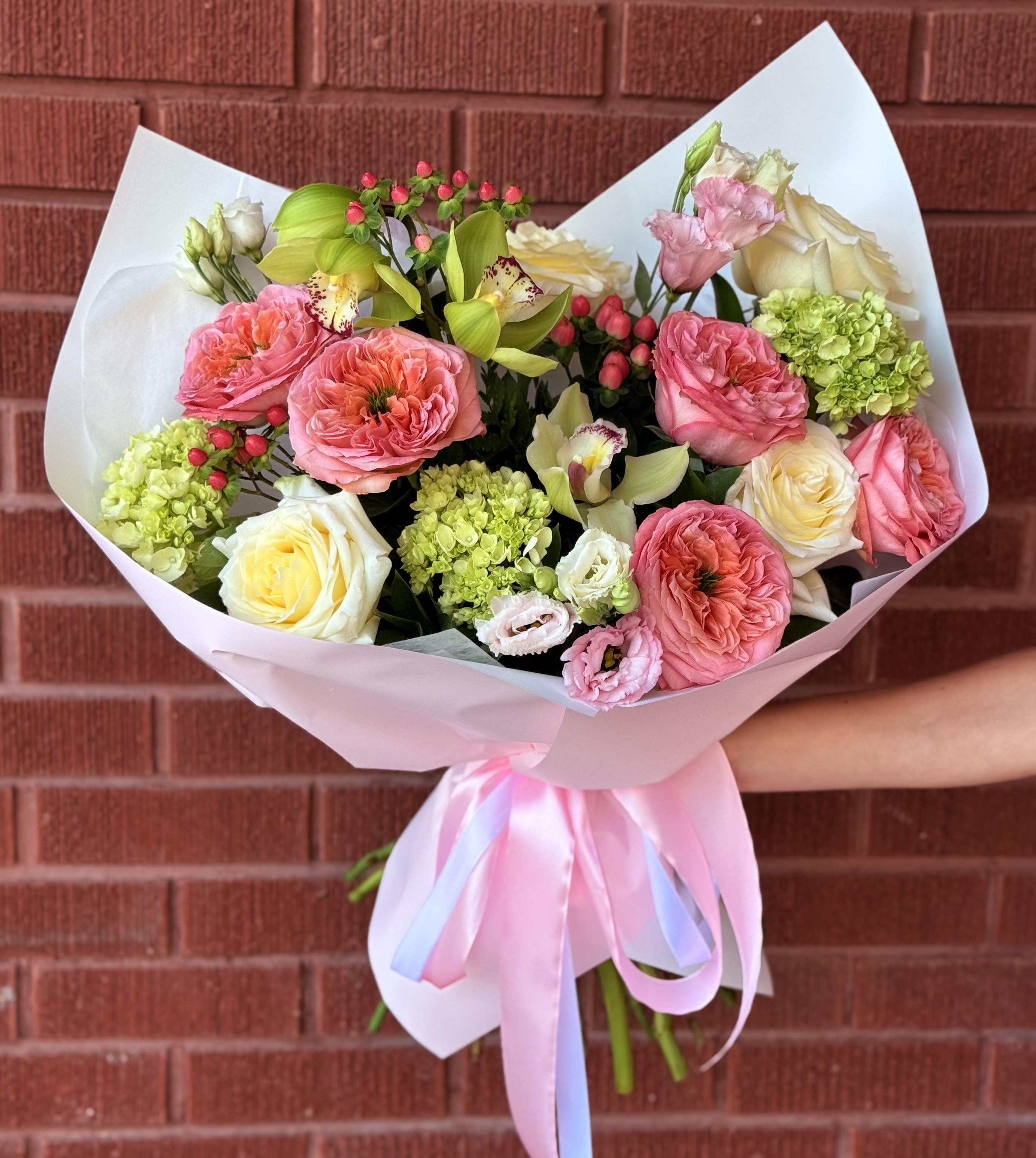 Bouquet of pink and cream flowers wrapped in pale paper with a ribbon