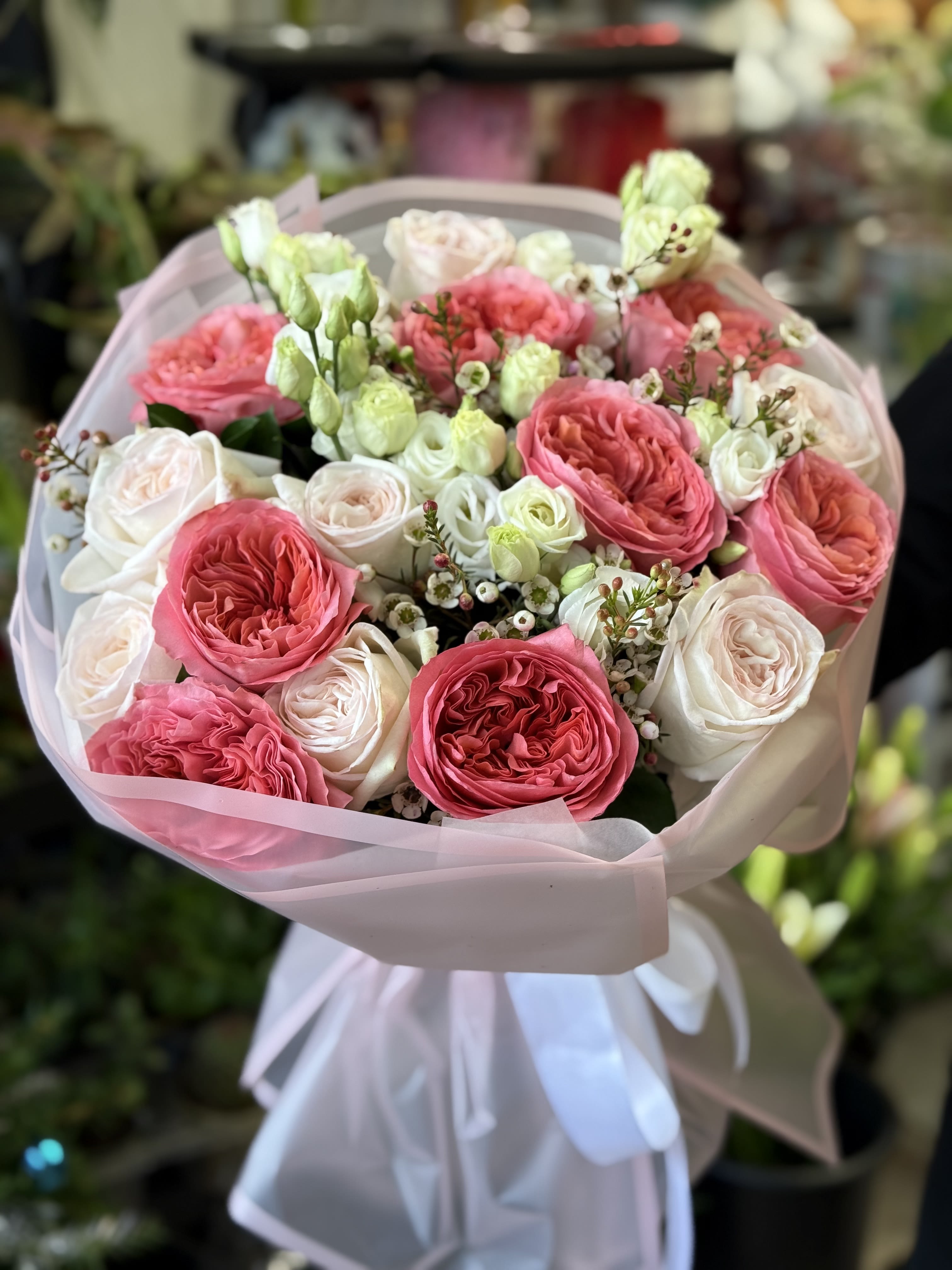 Pink and white rose bouquet wrapped in pale pink paper with a white ribbon