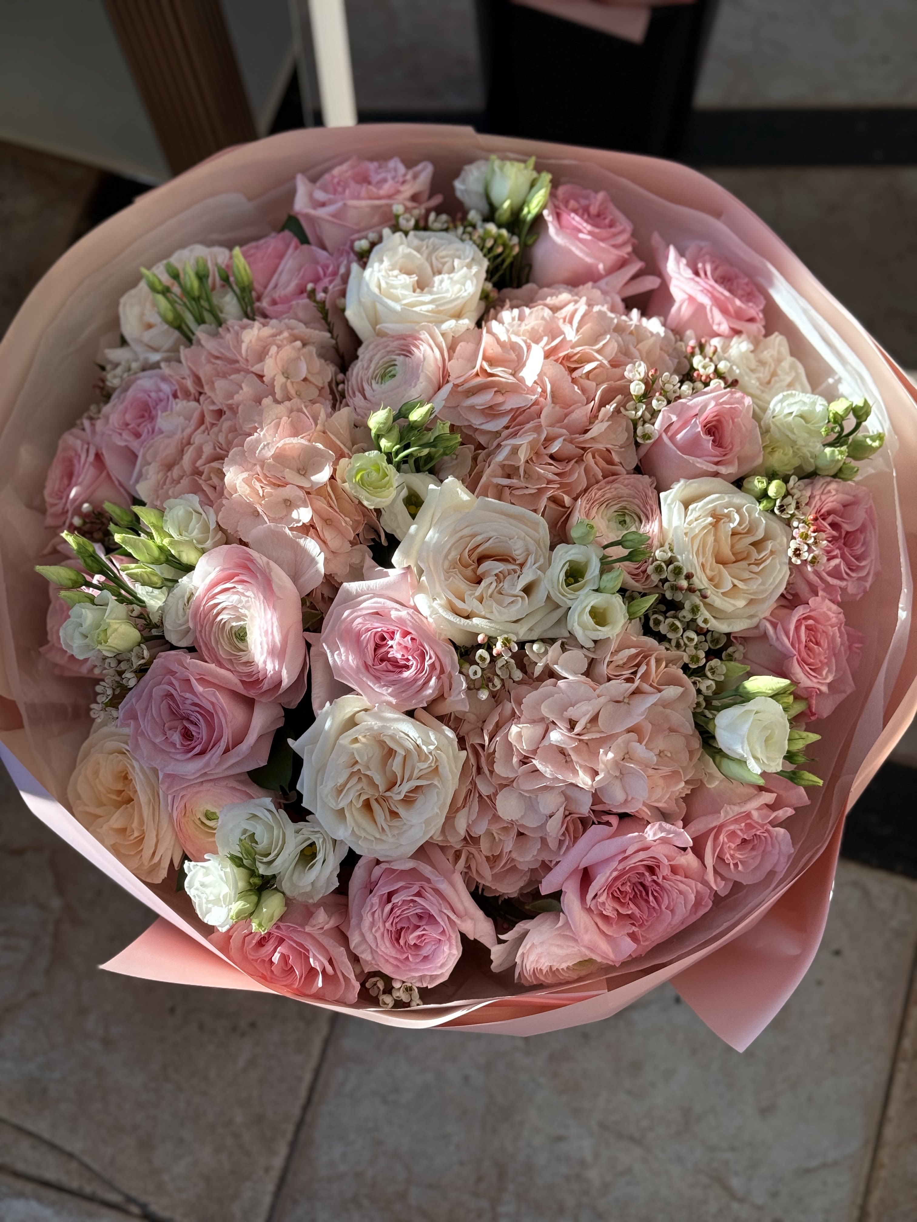 Pink and white bouquet of roses, hydrangeas, and ranunculus wrapped in pink paper