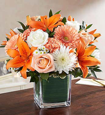 Orange lilies and peach roses in a clear square vase