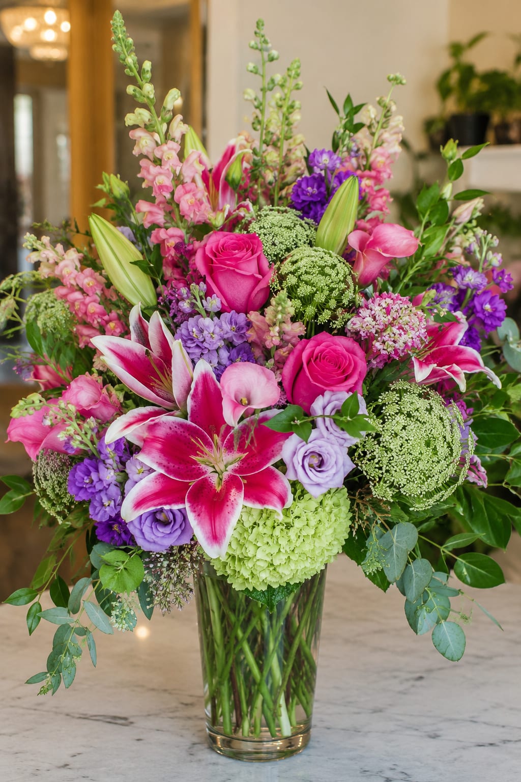 Meadow Of Light by Petal Perfection - Bright pink roses and pink-and-white lilies take center stage in this large, lush flower arrangement-an elegant birthday bouquet or anniversary arrangement that reads as both romantic and celebratory. Lavender and purple blooms add depth while pale green hydrangea-like clusters and airy filler flowers soften the overall look, so the person you're sending it to will feel truly seen and celebrated the moment it arrives.  Carefully layered for a polished silhouette, this mixed arrangement features lilies, roses, hydrangea-like clusters, stock, calla lilies and additional seasonal blooms arranged in a clear glass vase. Tall stems rise above a dense, textured center with trailing greenery at the edges for graceful movement; the palette blends pink, purple, white and green for a fresh, garden-inspired impression.  Perfect for marking birthdays, anniversaries, or a special congratulations, this is the kind of bouquet that reads as both thoughtful and luxurious for the recipient. Delivered ready-to-display in its vase-trim stems and change water every 2-3 days to prolong freshness and keep the arrangement looking its best.