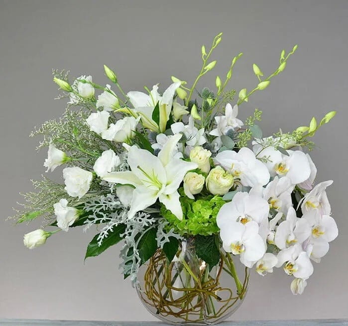White floral arrangement in a clear glass vase with orchids and lilies
