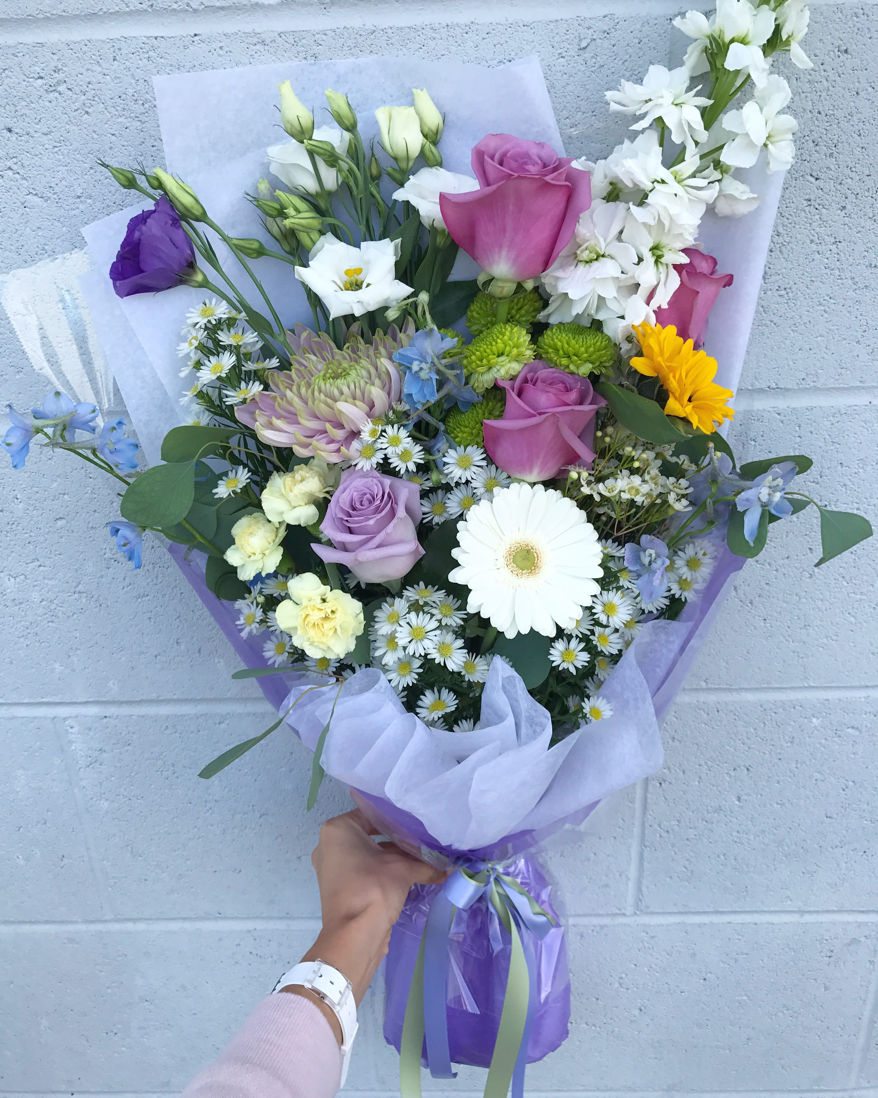 Handheld bouquet of mixed flowers in purple wrapping