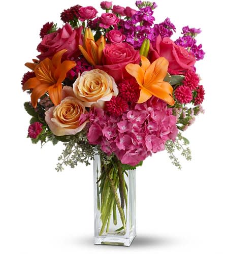 Mixed bouquet of roses, lilies, hydrangea, and orange blooms in a glass vase