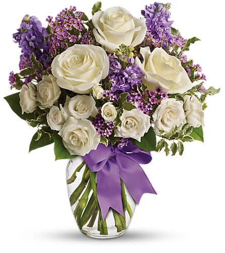 White roses and purple flowers in a glass vase with a purple ribbon